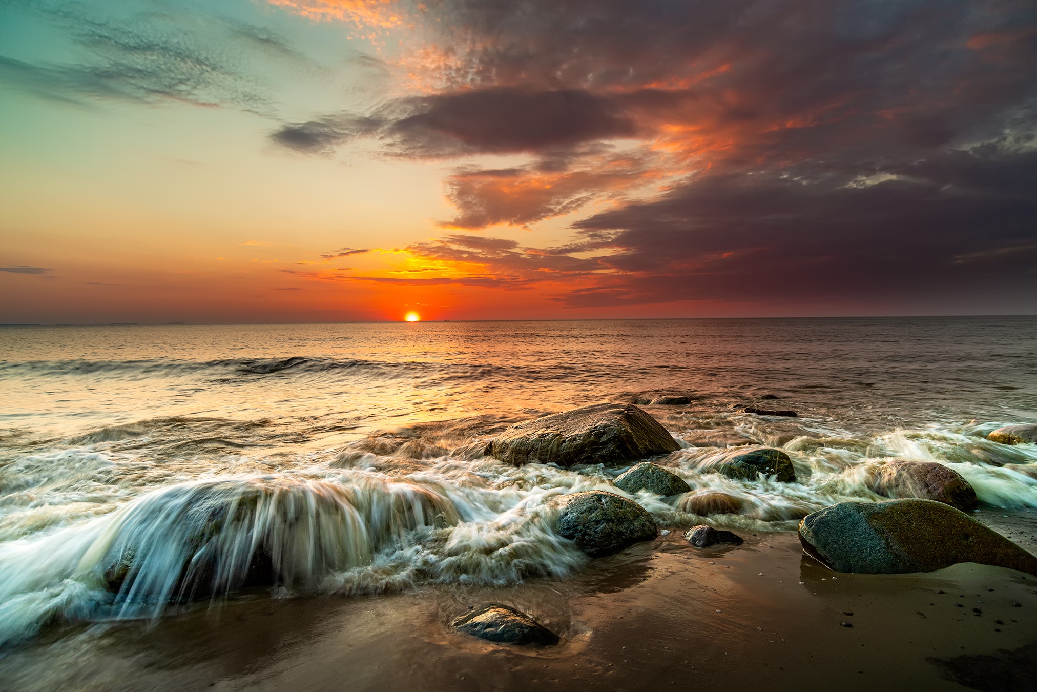 Sunset over the ocean with waves crashing on rocks HD Wallpaper