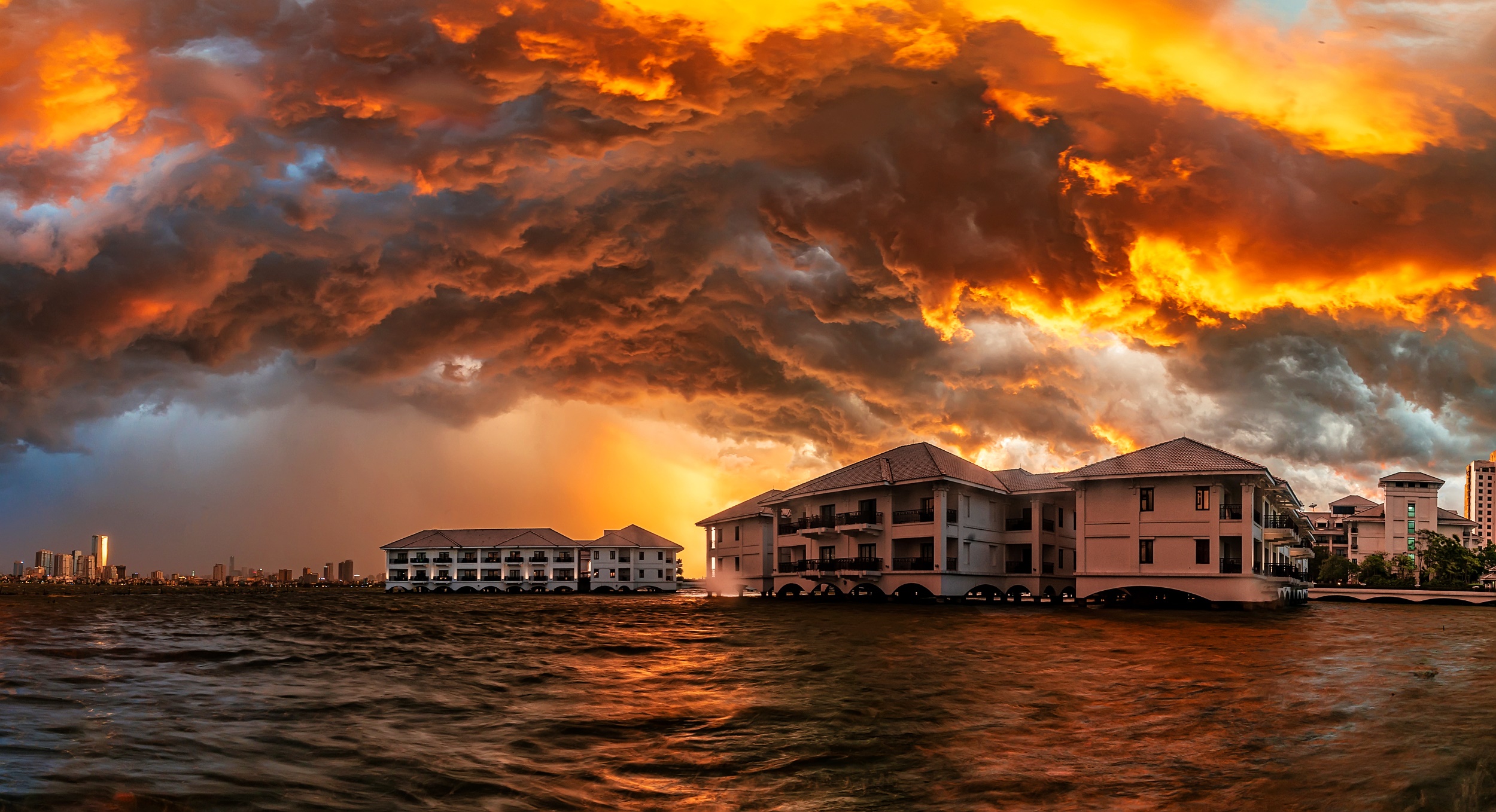 Resort buildings on water under dramatic sunset clouds HD Wallpaper