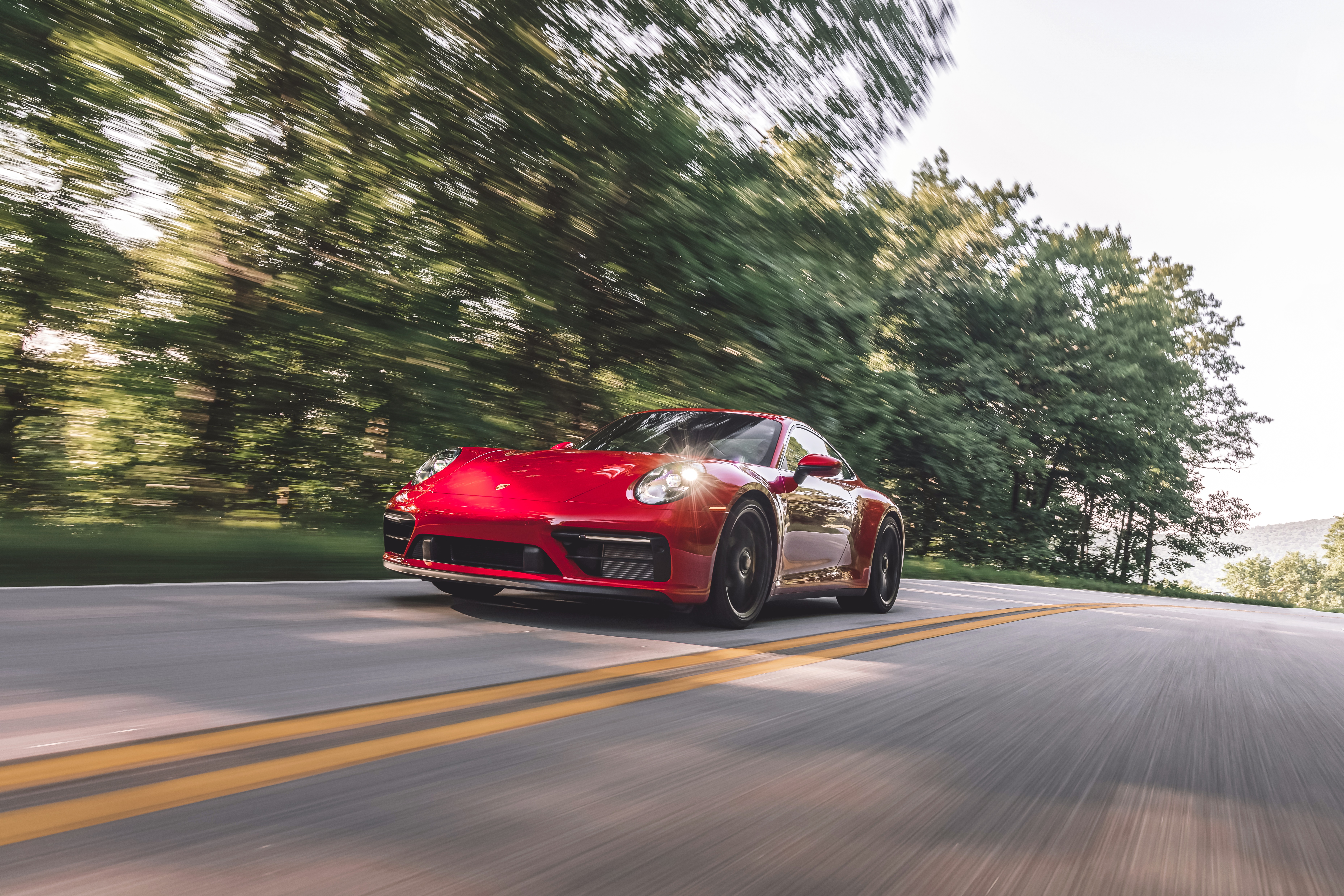 Red Porsche 911 Carrera GTS driving on a tree-lined road HD Wallpaper