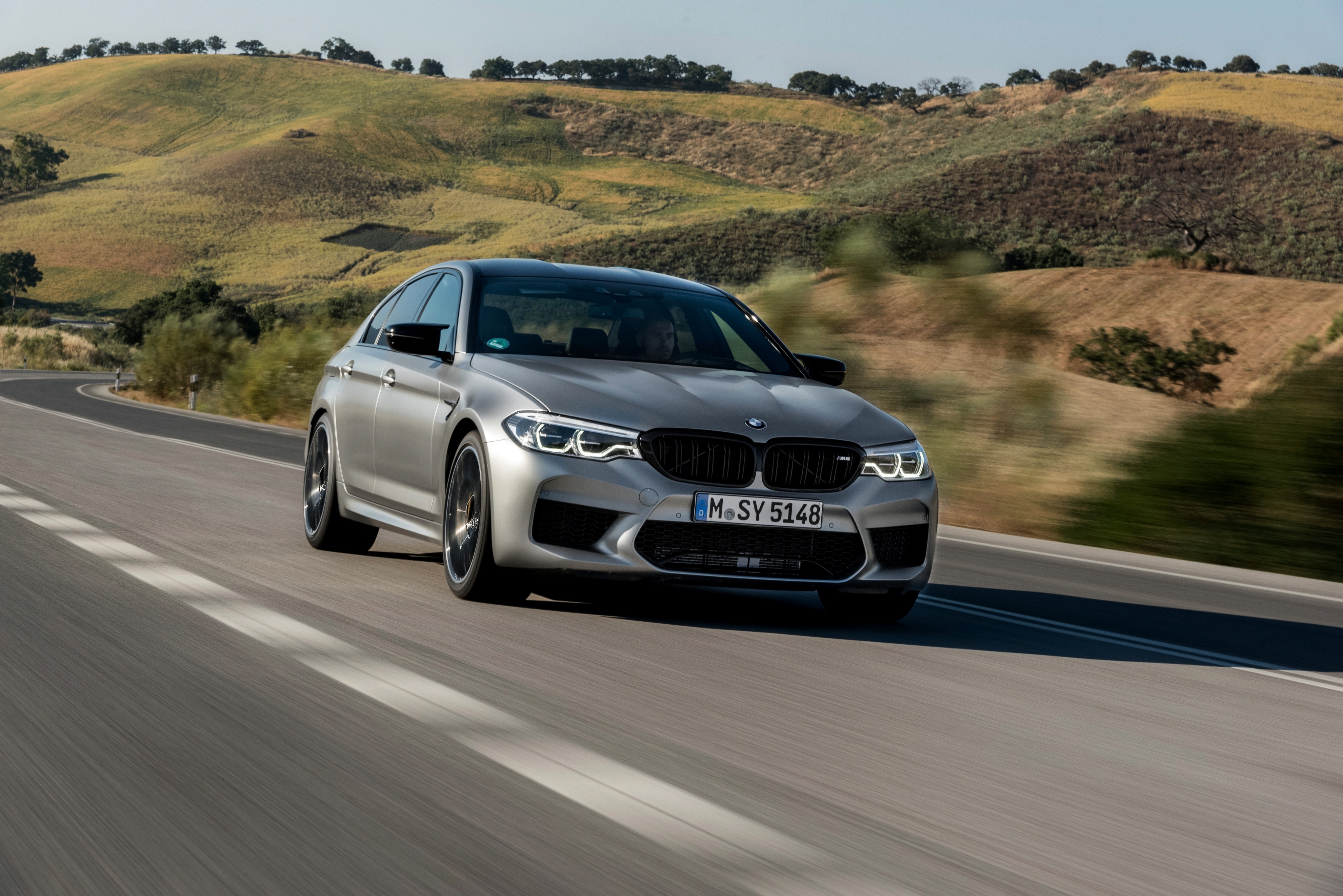 Silver BMW M5 Competition driving on a road HD Wallpaper