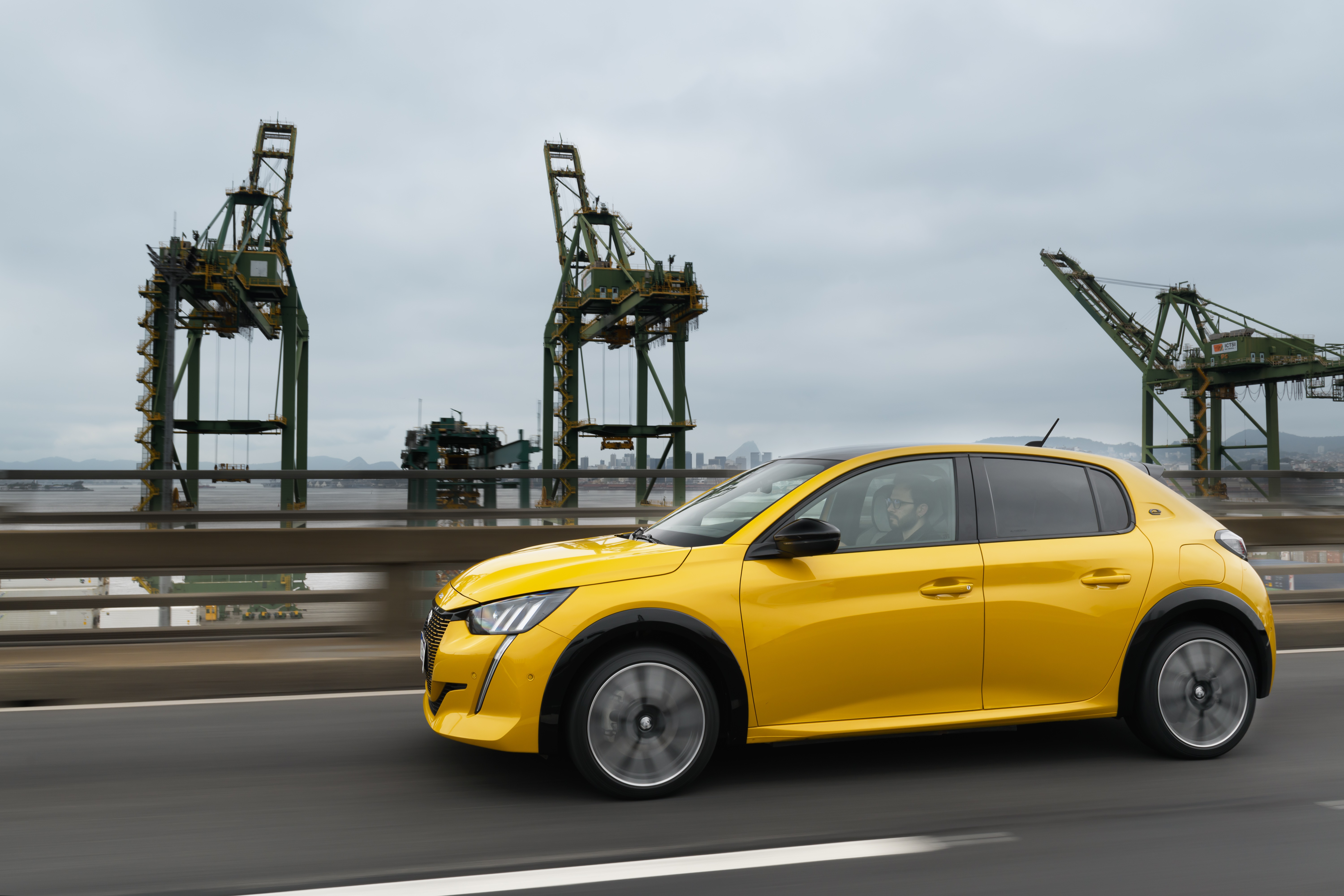 Yellow Peugeot E-208 GT driving on a bridge HD Wallpaper
