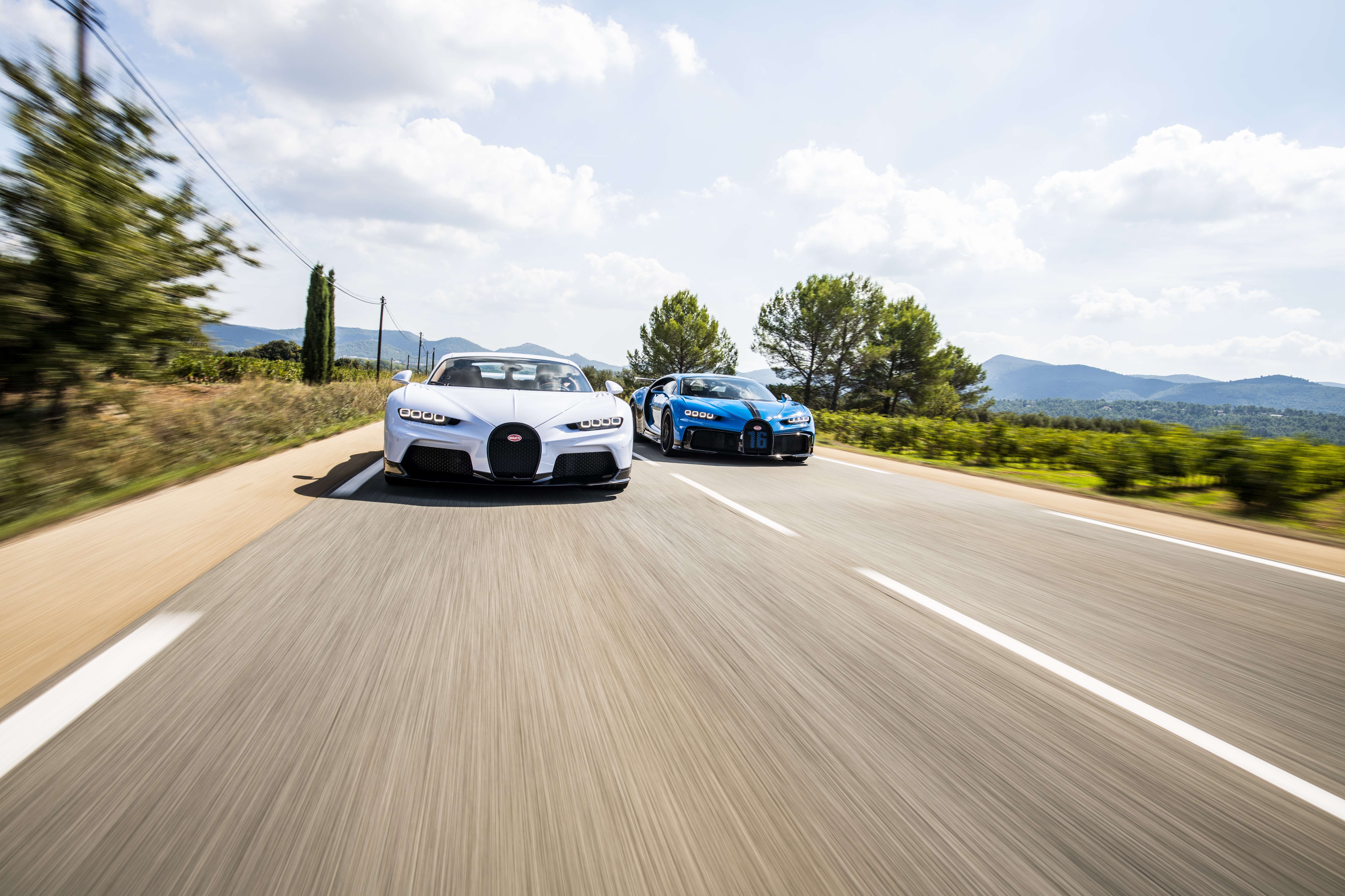 Two Bugatti Chirons driving on a road HD Wallpaper
