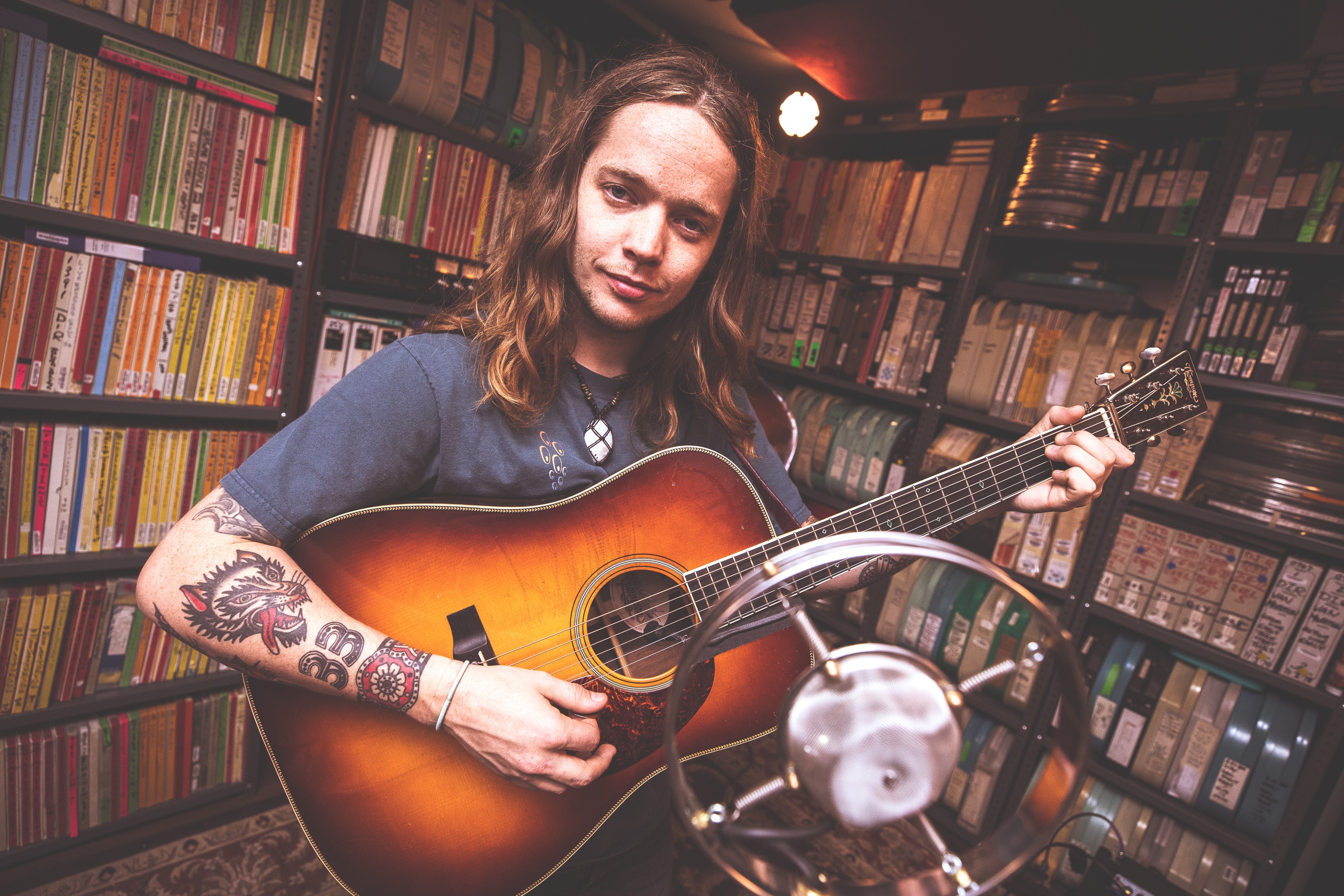 Billy Strings playing guitar in front of bookshelves HD Wallpaper