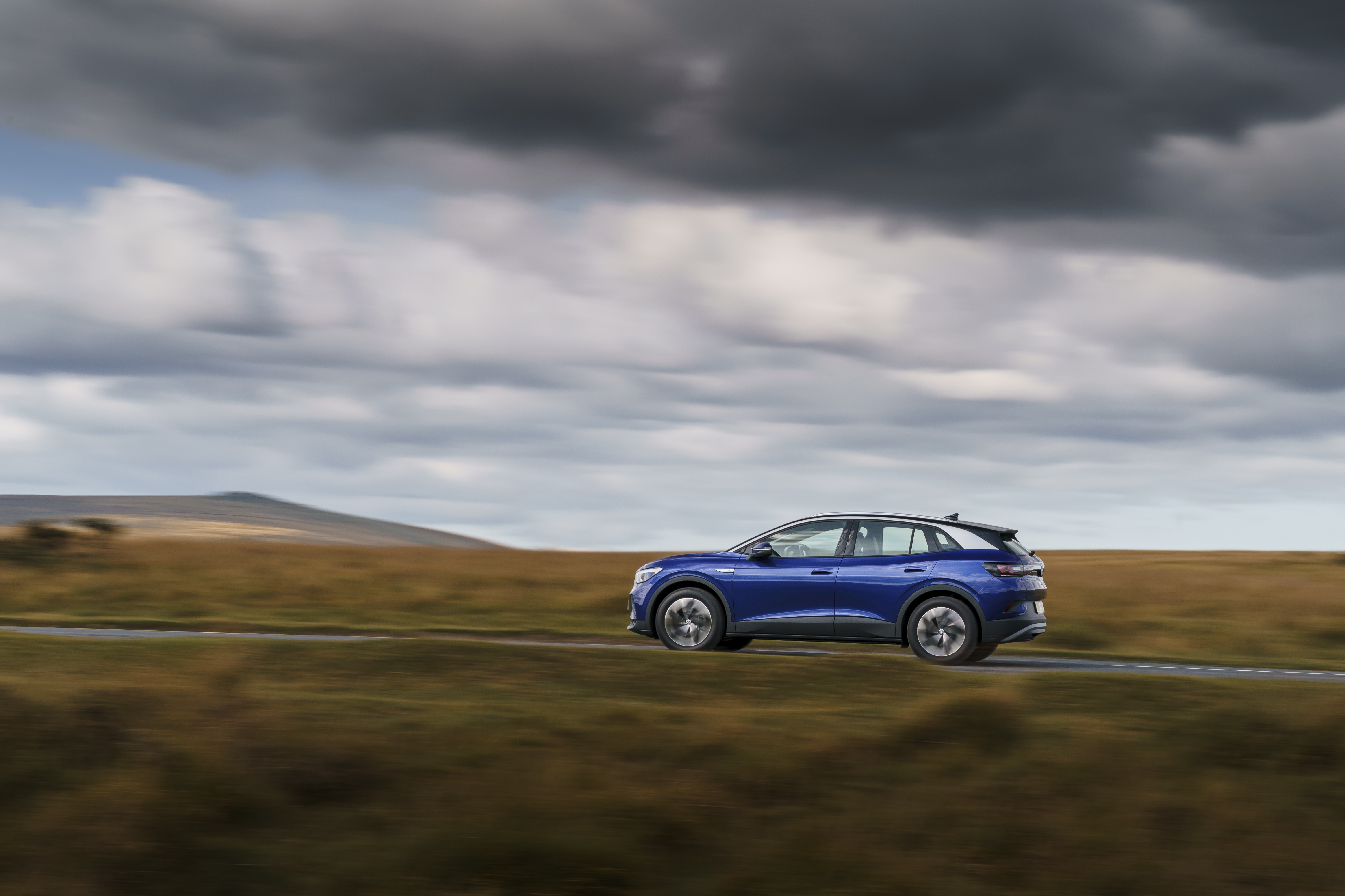 Blue Volkswagen ID.4 electric car driving on a road HD Wallpaper