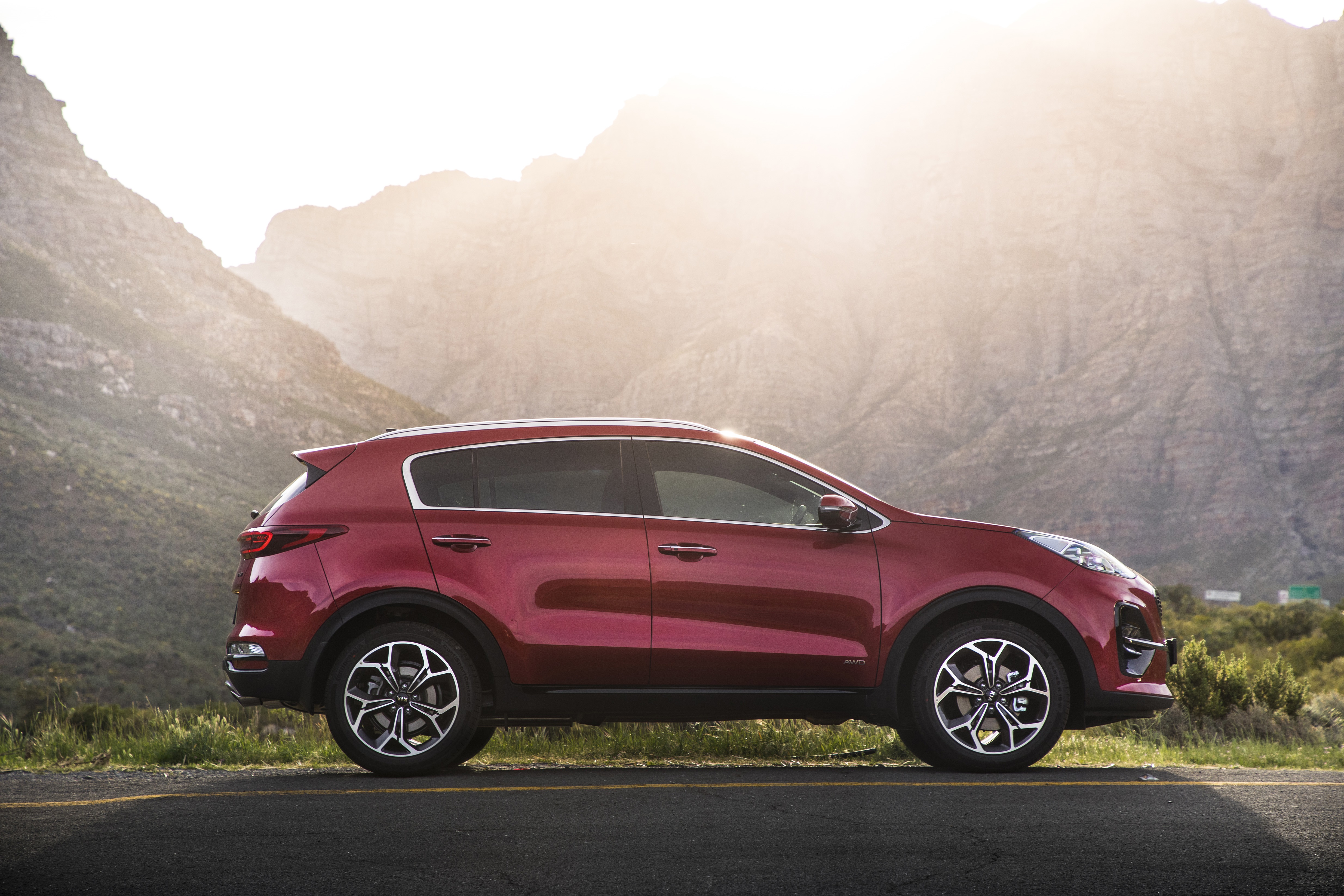 Red Kia Sportage SUV parked on a road with mountains HD Wallpaper