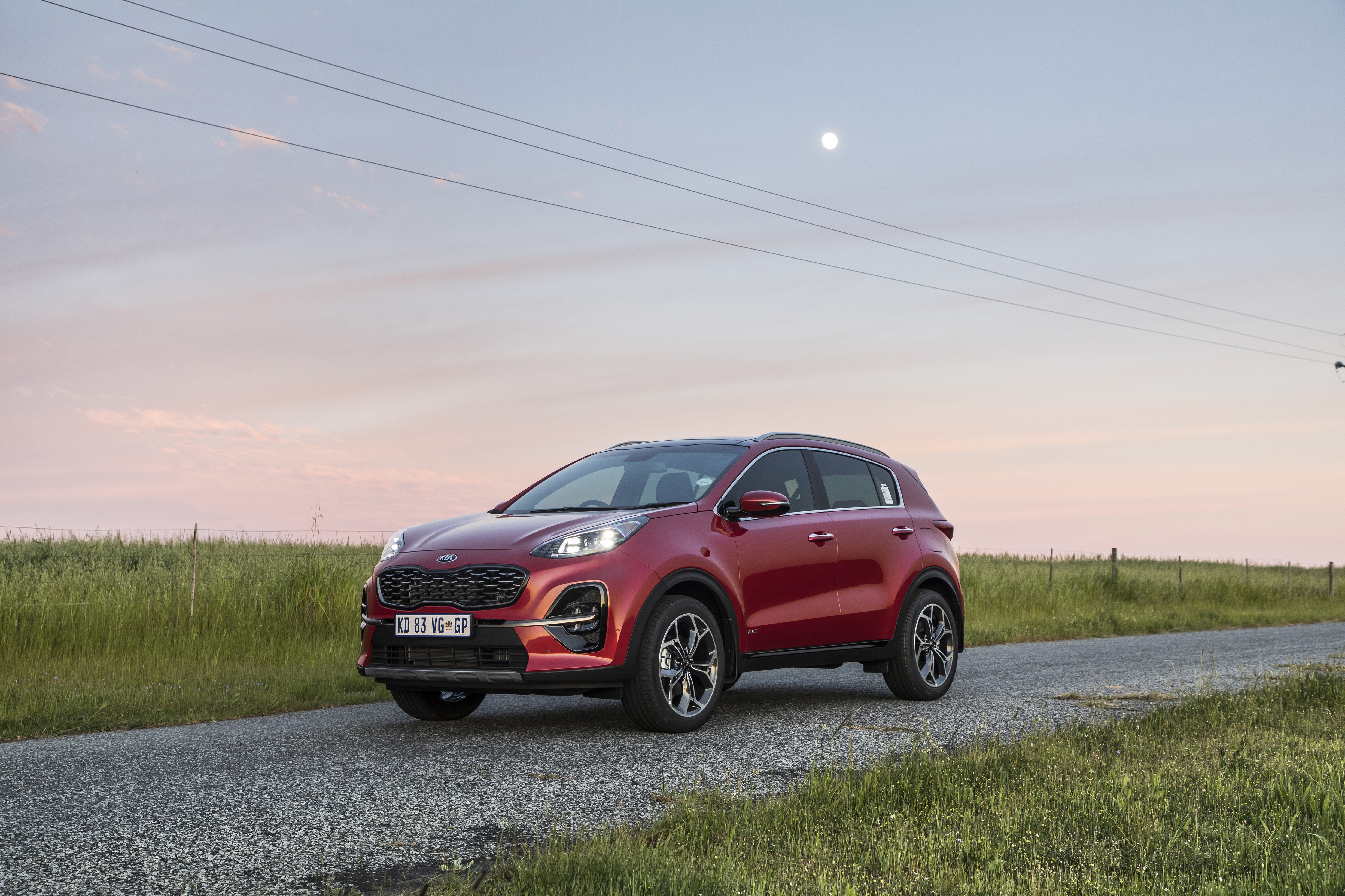 Red Kia Sportage SUV on a road at sunset HD Wallpaper