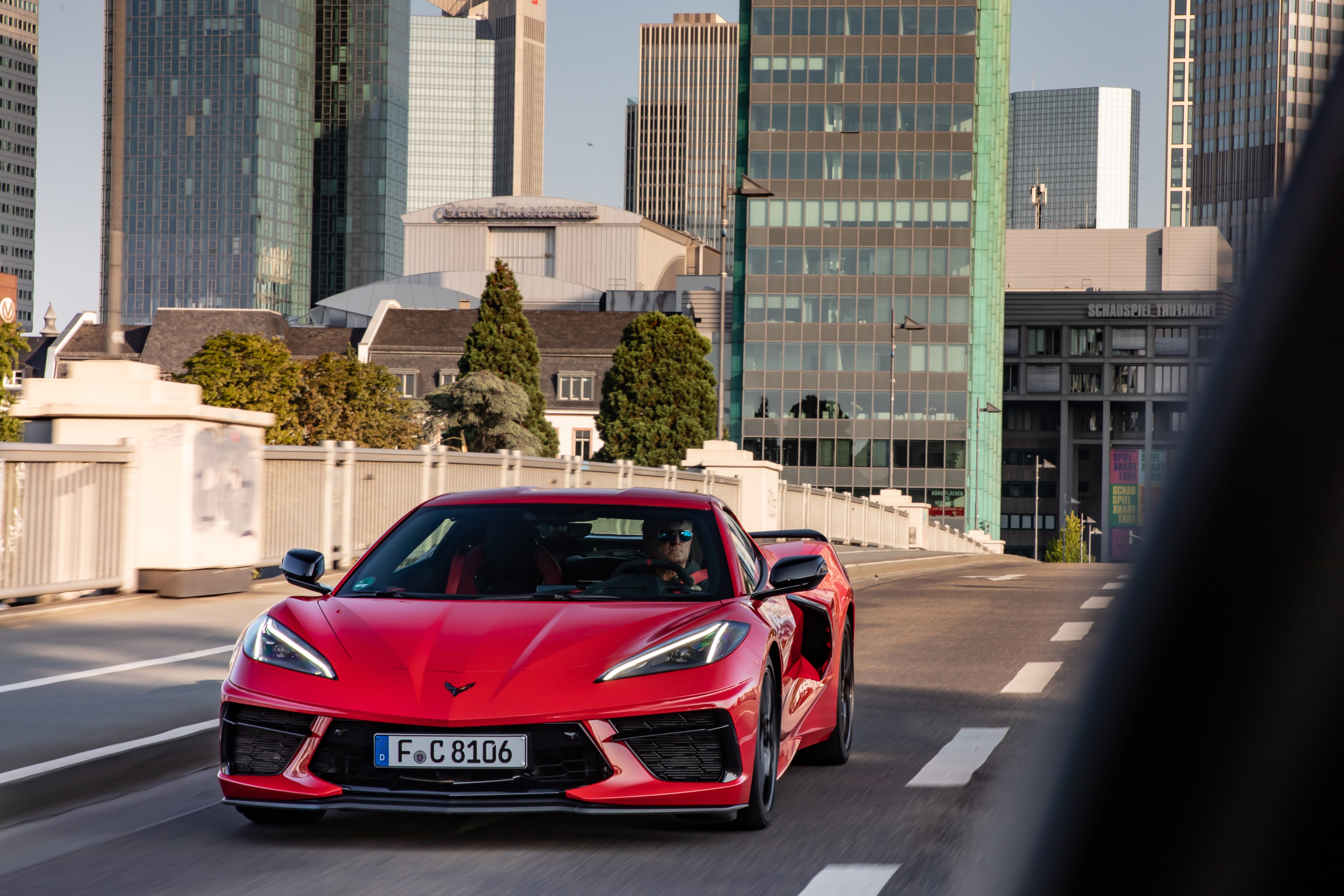 Red Chevrolet Corvette (C8) driving in city HD Wallpaper