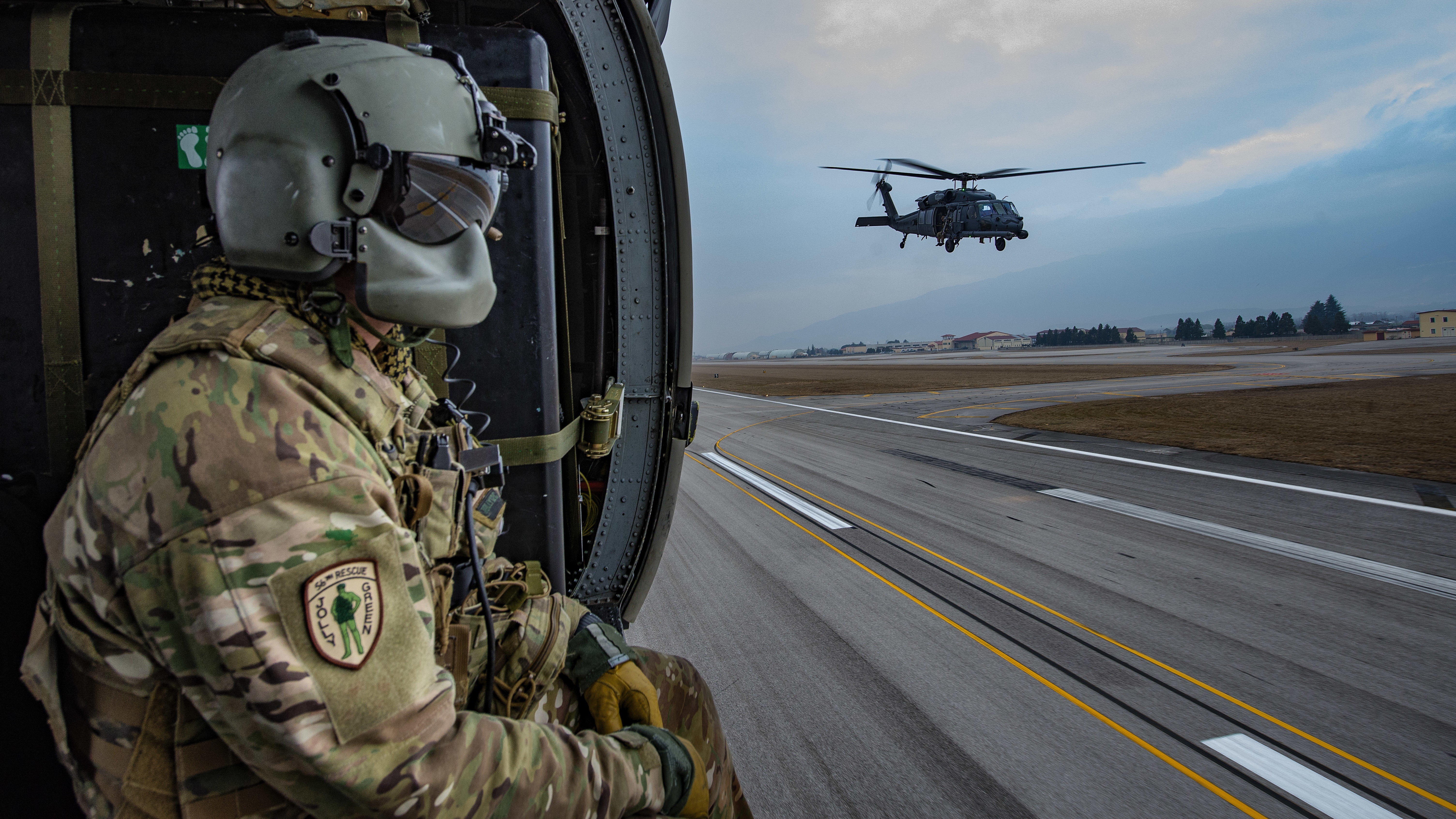 Soldier in helicopter watches another helicopter take off HD Wallpaper