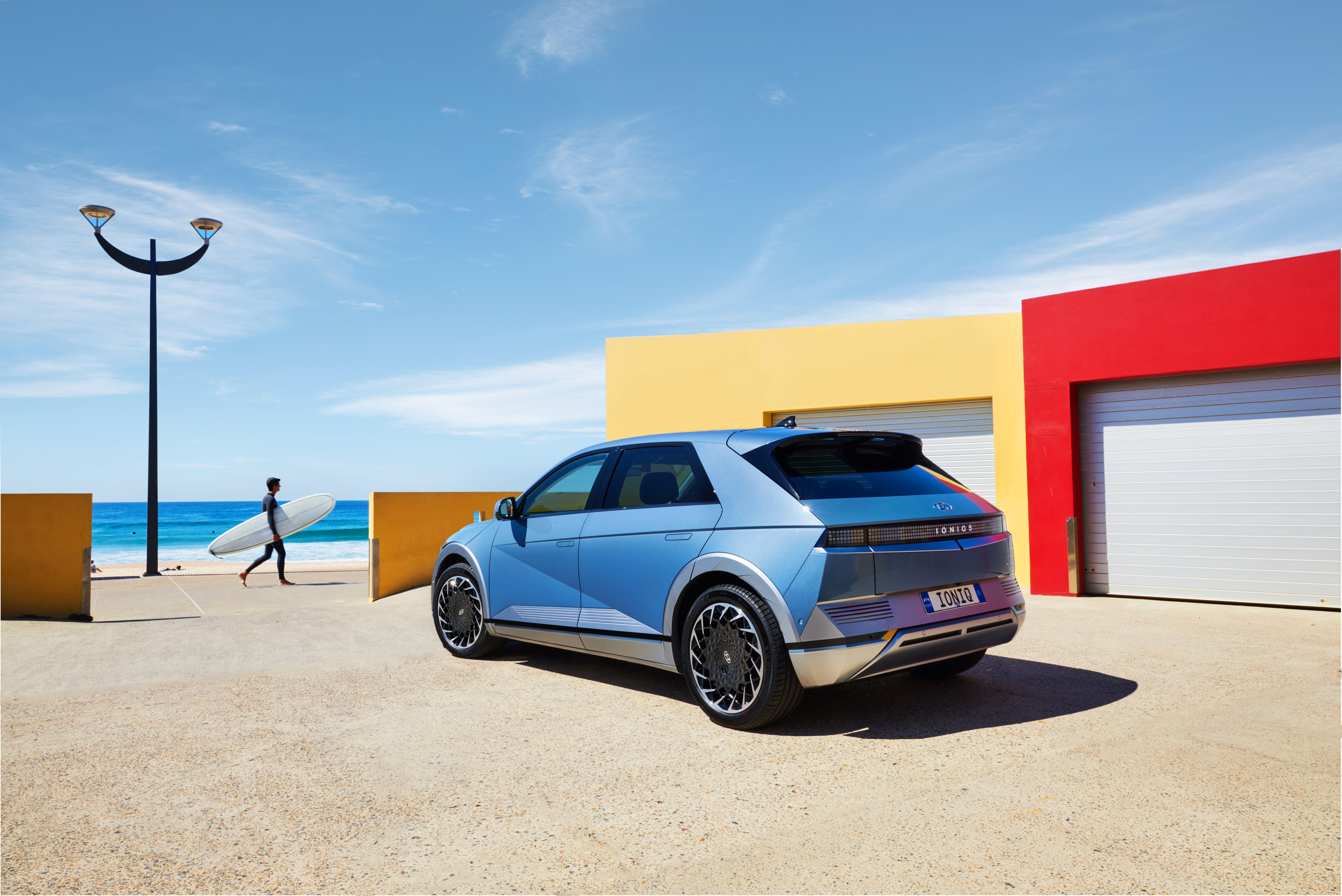 Blue Hyundai Ioniq 5 parked near colorful buildings by the ocean HD Wallpaper