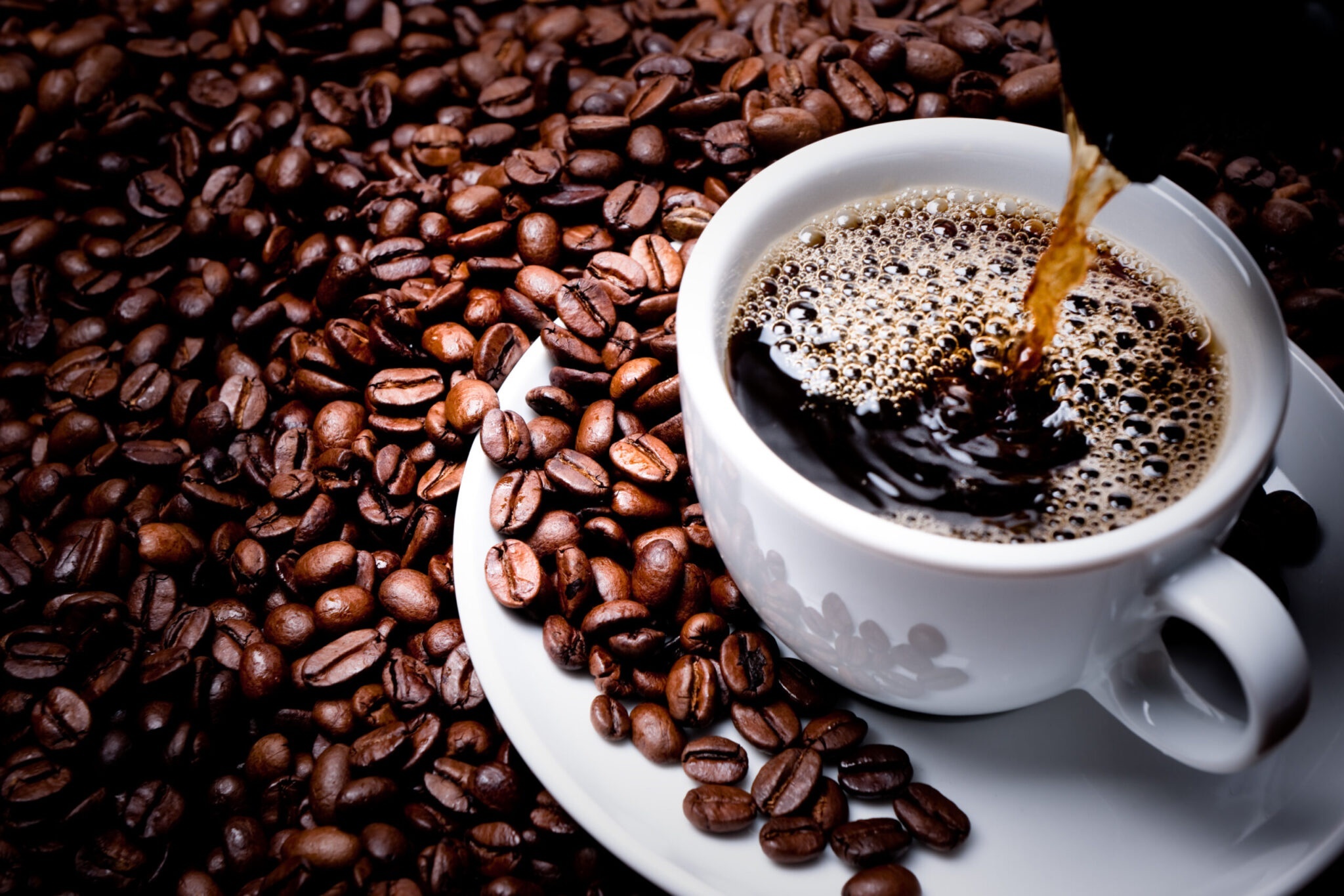 Coffee poured into a cup surrounded by coffee beans HD Wallpaper