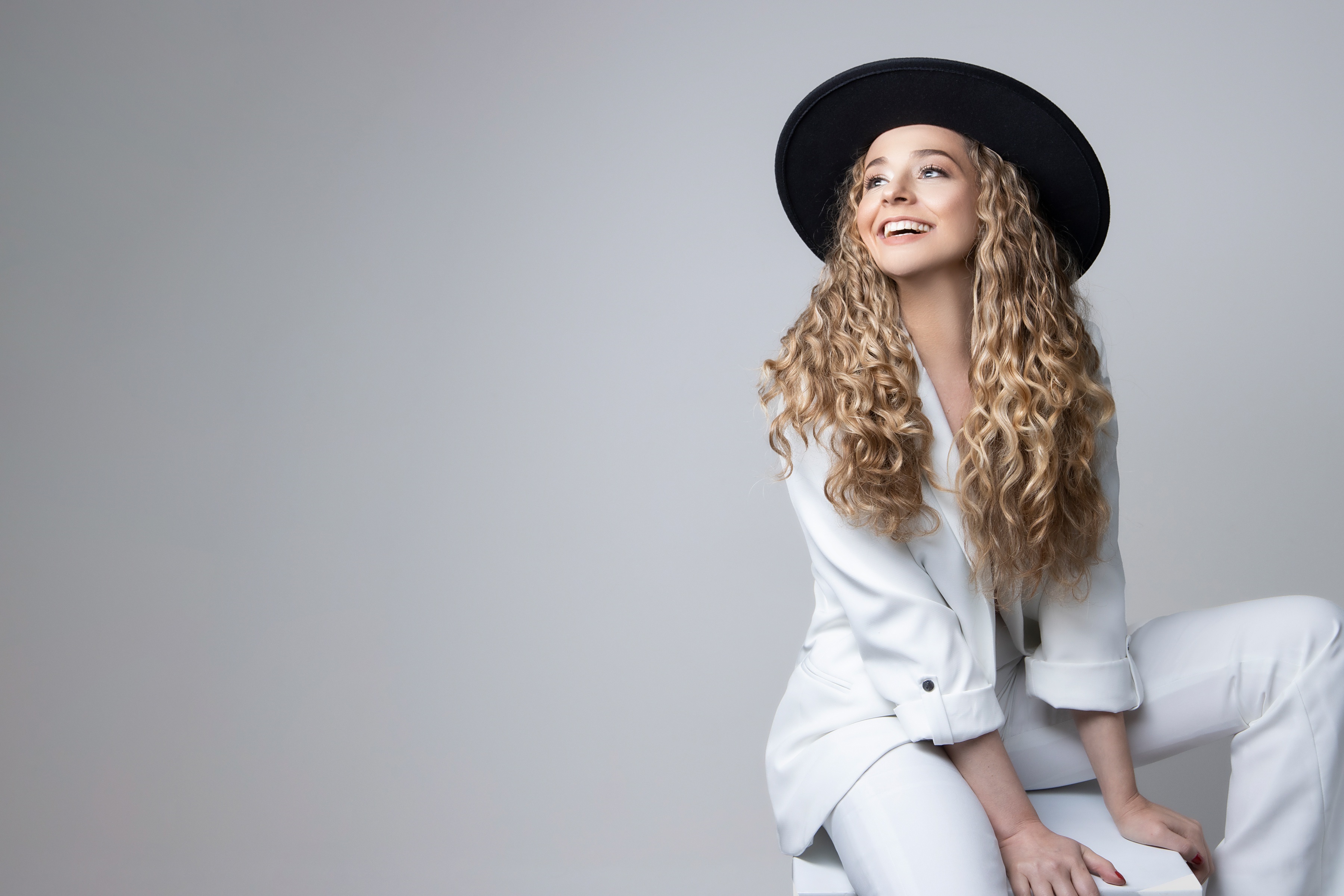 Woman with curly hair wearing a hat and white suit HD Wallpaper