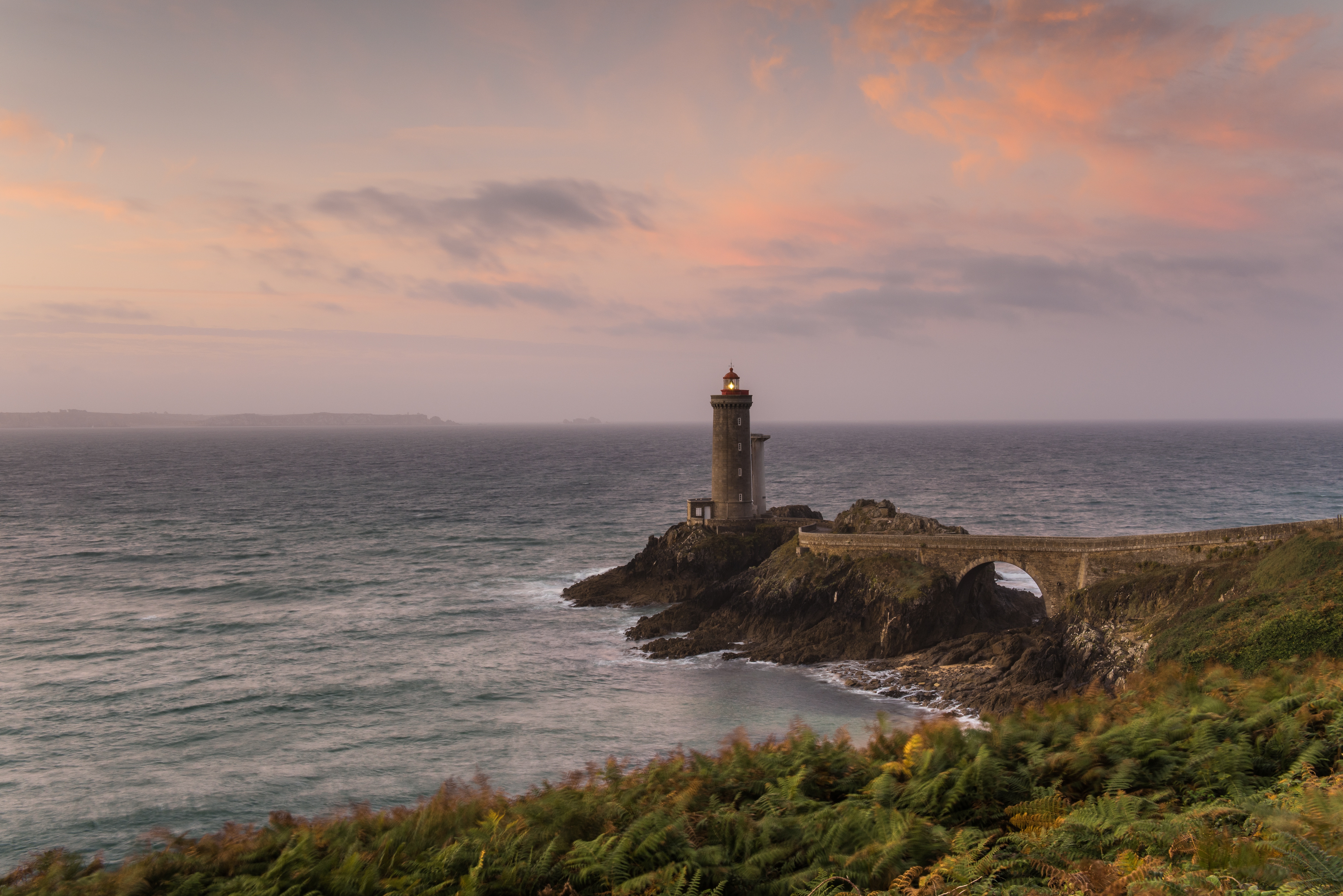 Lighthouse on a rocky coast at sunset HD Wallpaper