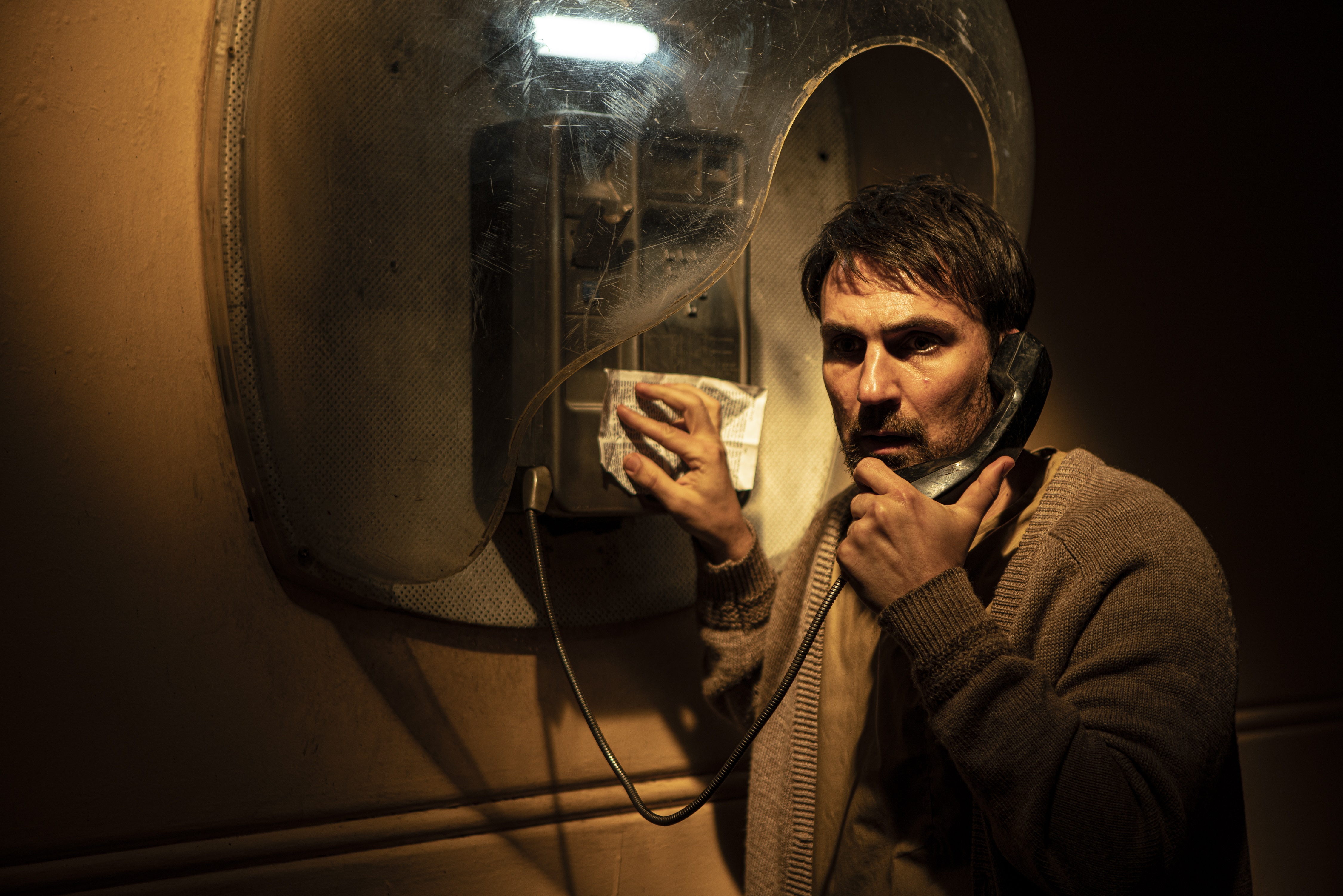 Man using a payphone in a dimly lit room HD Wallpaper