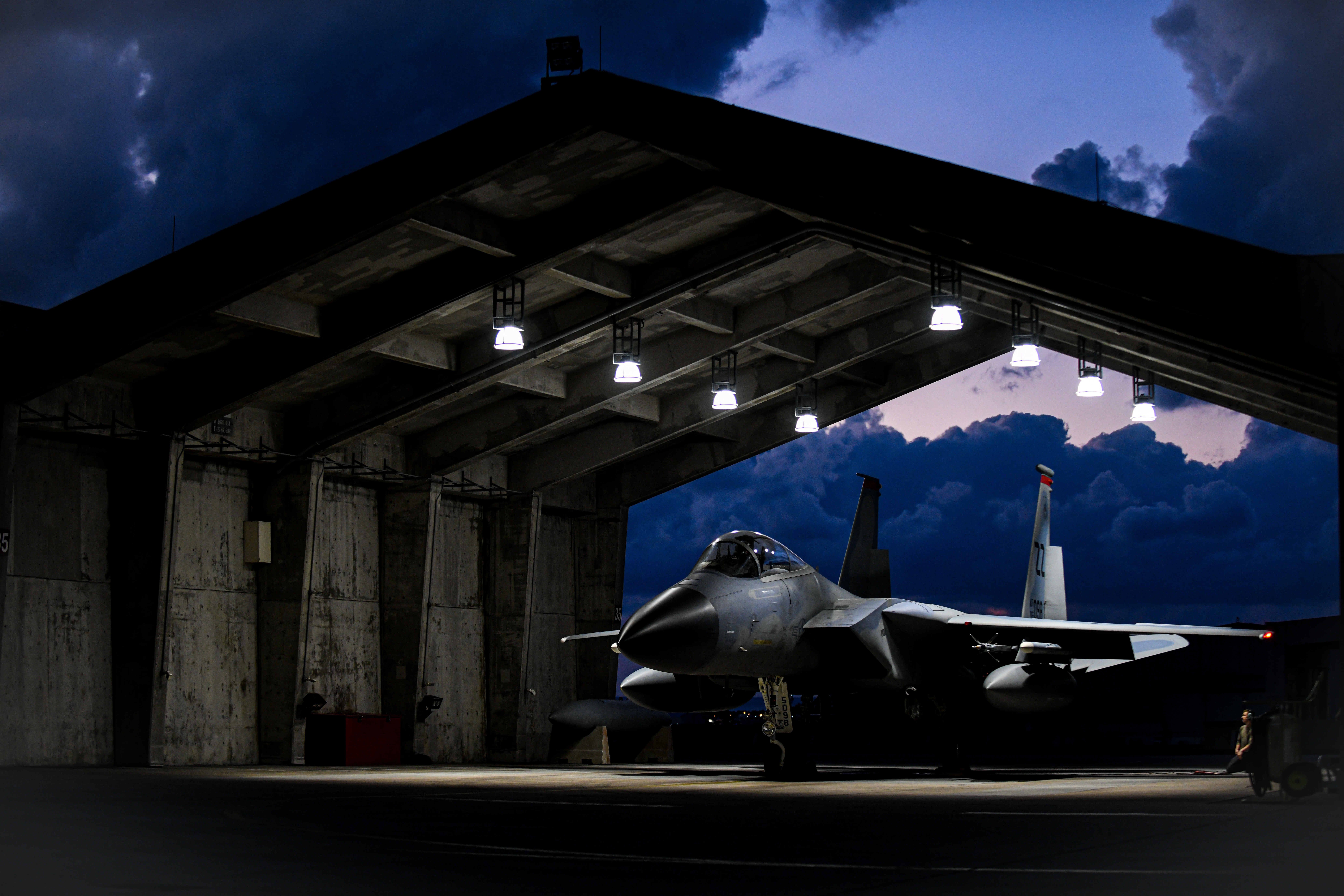 F-15 Eagle fighter jet in a hangar at dusk HD Wallpaper