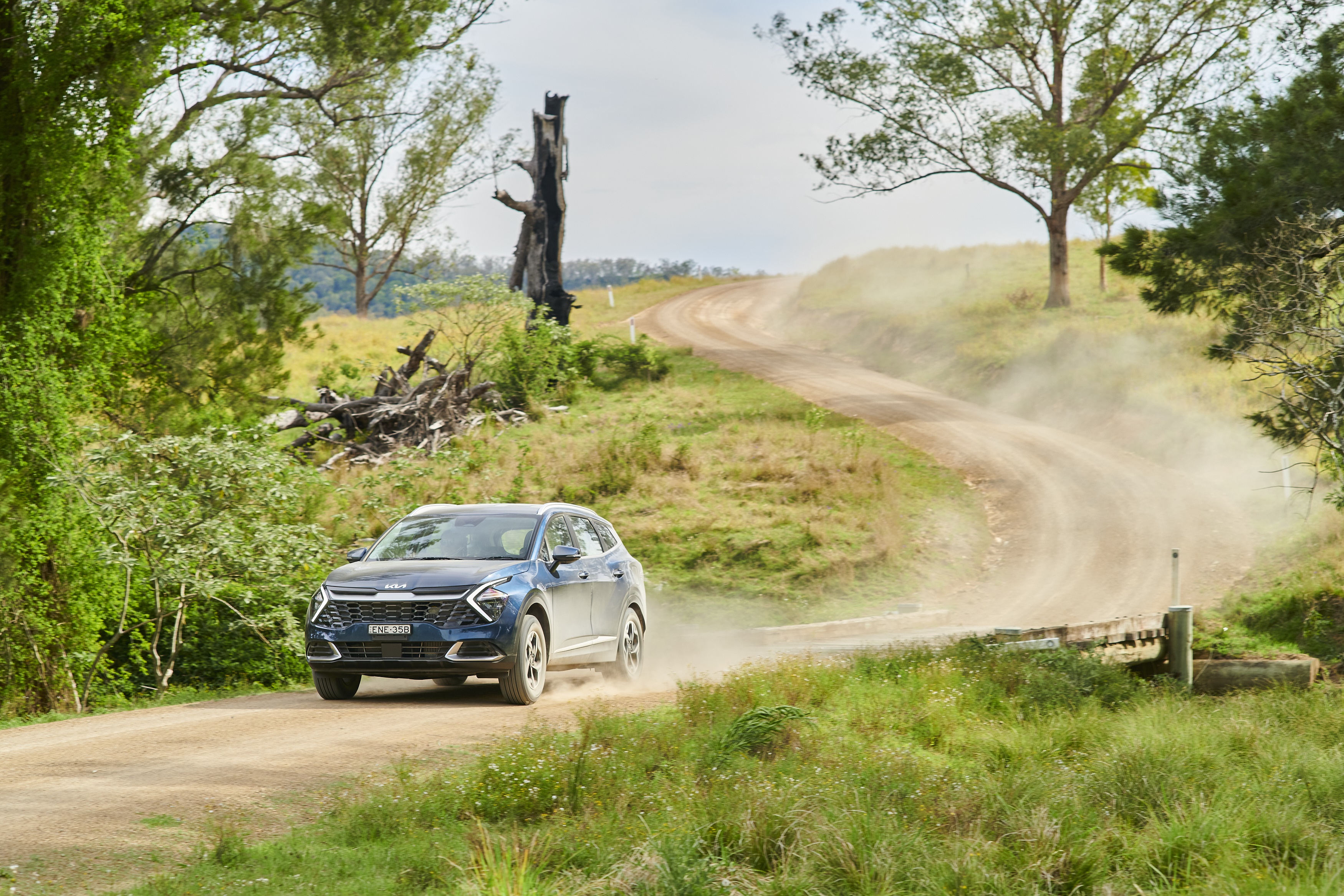 Blue Kia Sportage driving on a dusty rural road HD Wallpaper