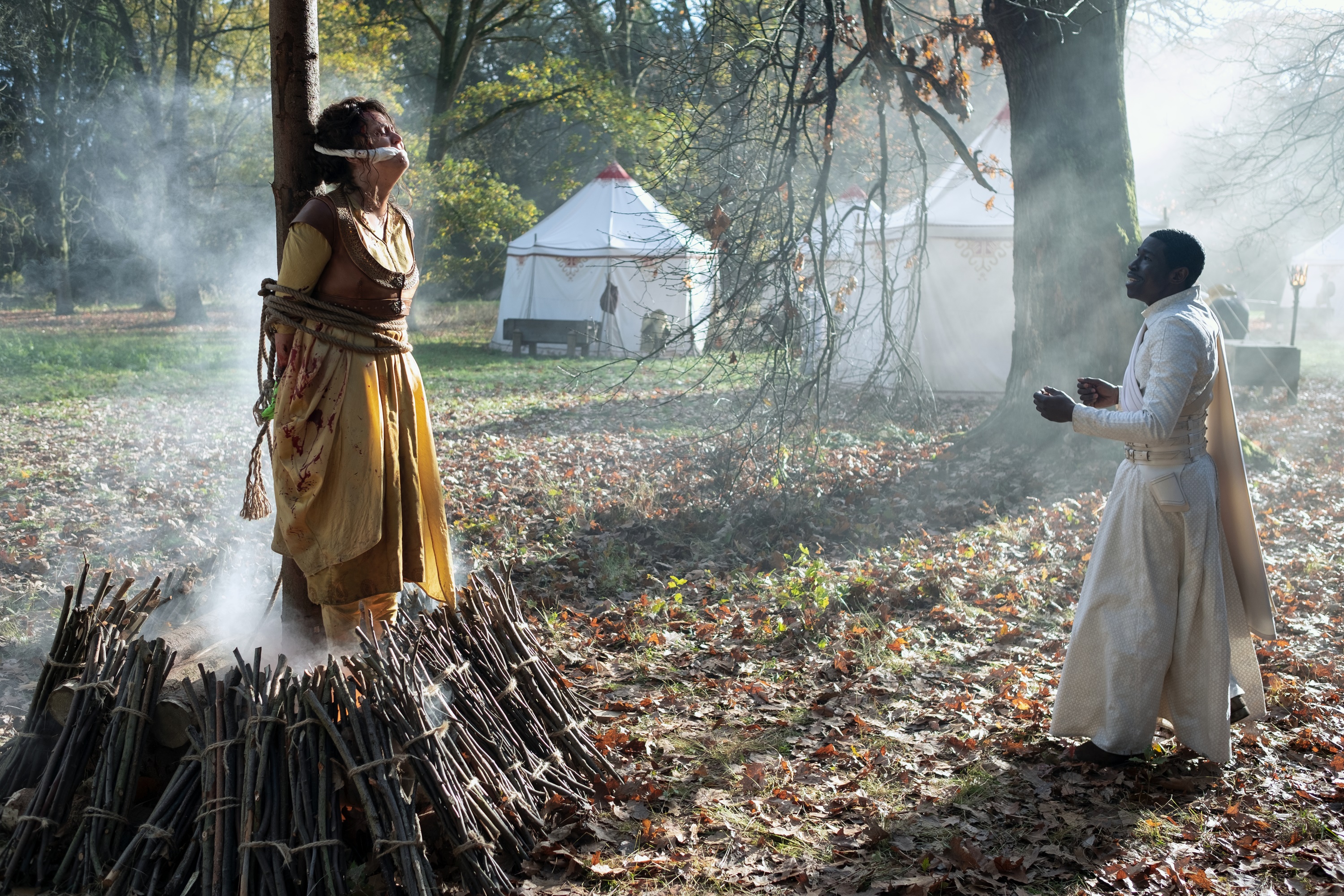 Woman tied to tree with fire pit, man in white robes HD Wallpaper