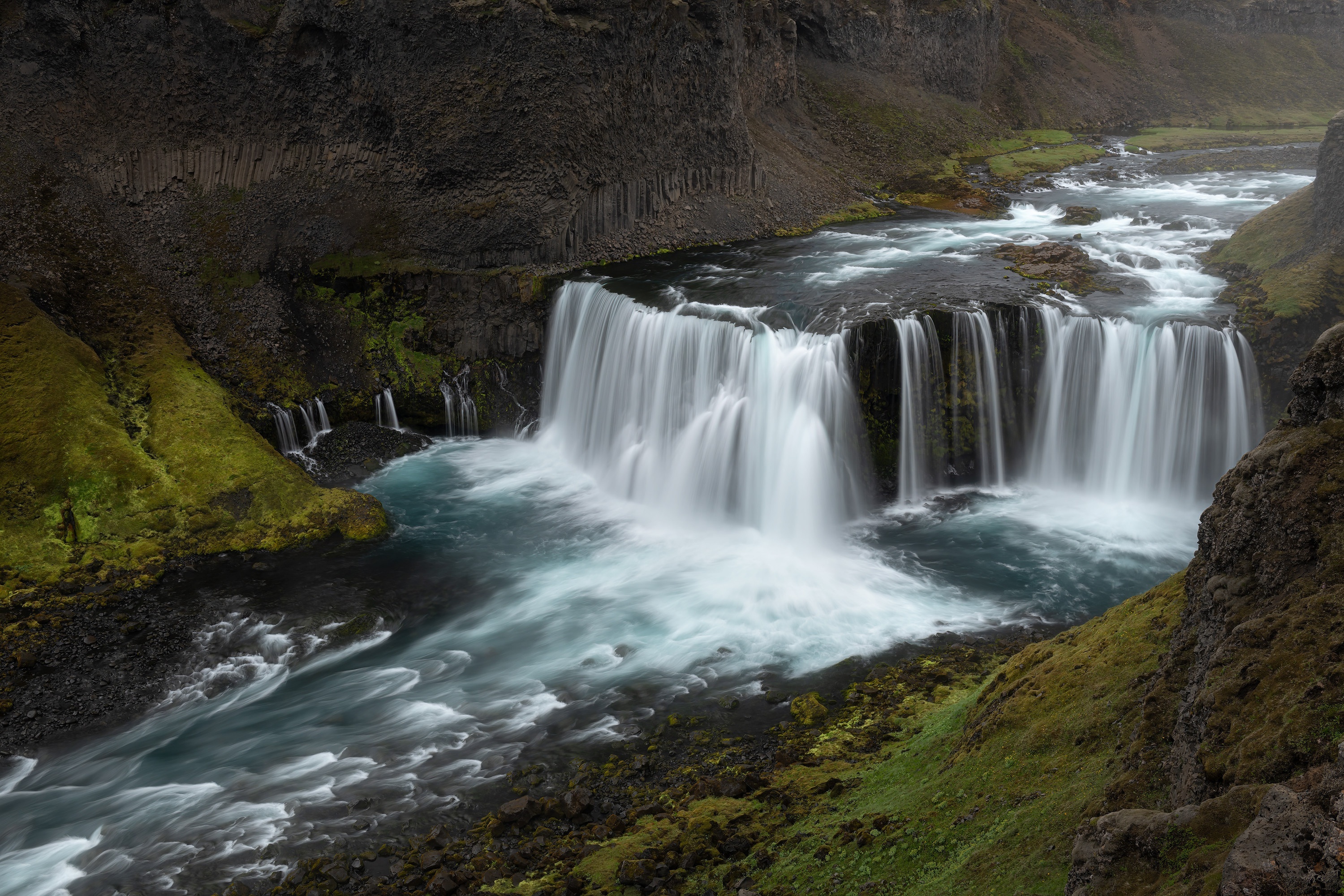 Wide waterfall cascading into a river in a rocky canyon HD Wallpaper