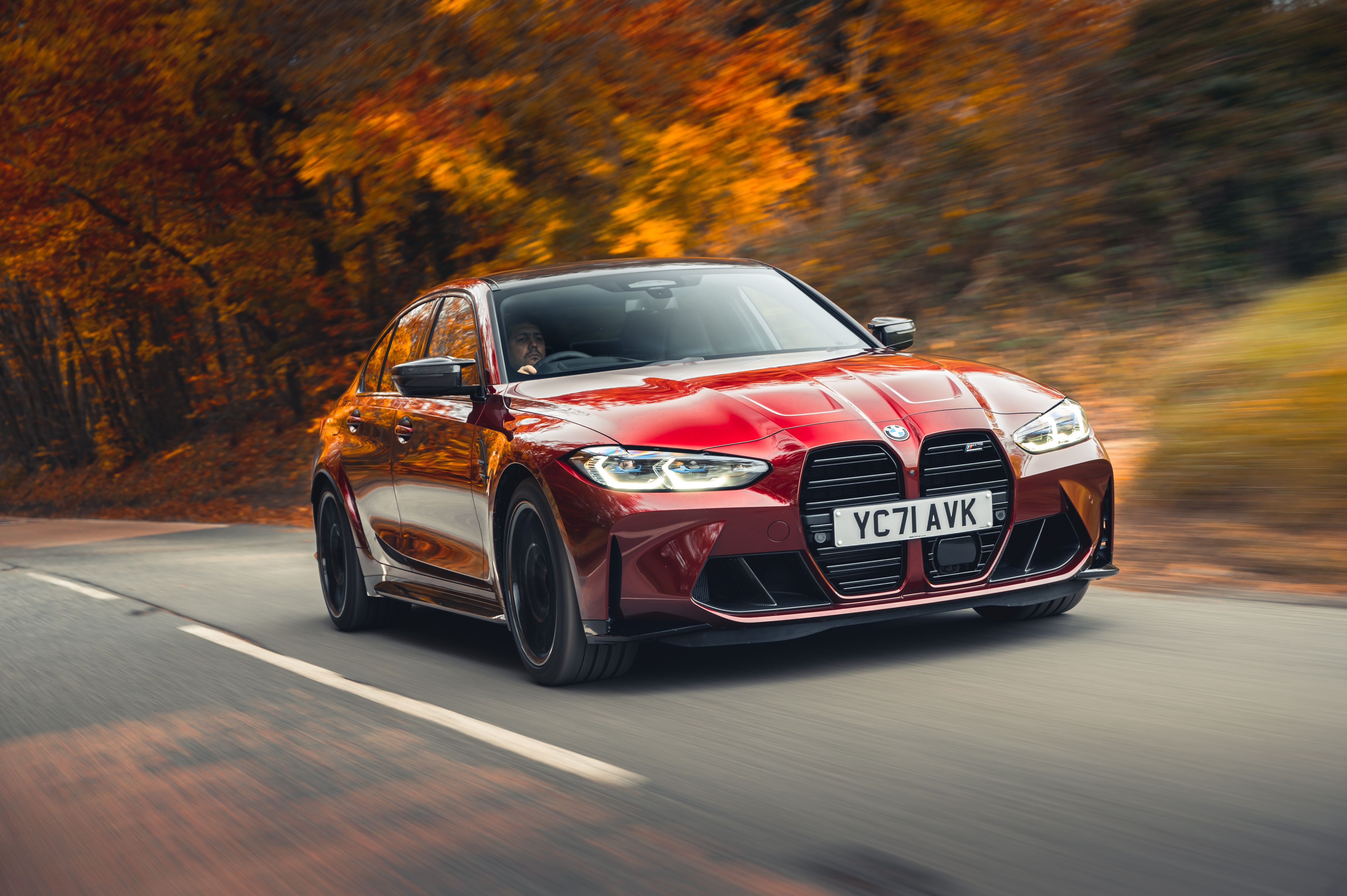 Red BMW M3 Competition driving on a road with autumn trees HD Wallpaper