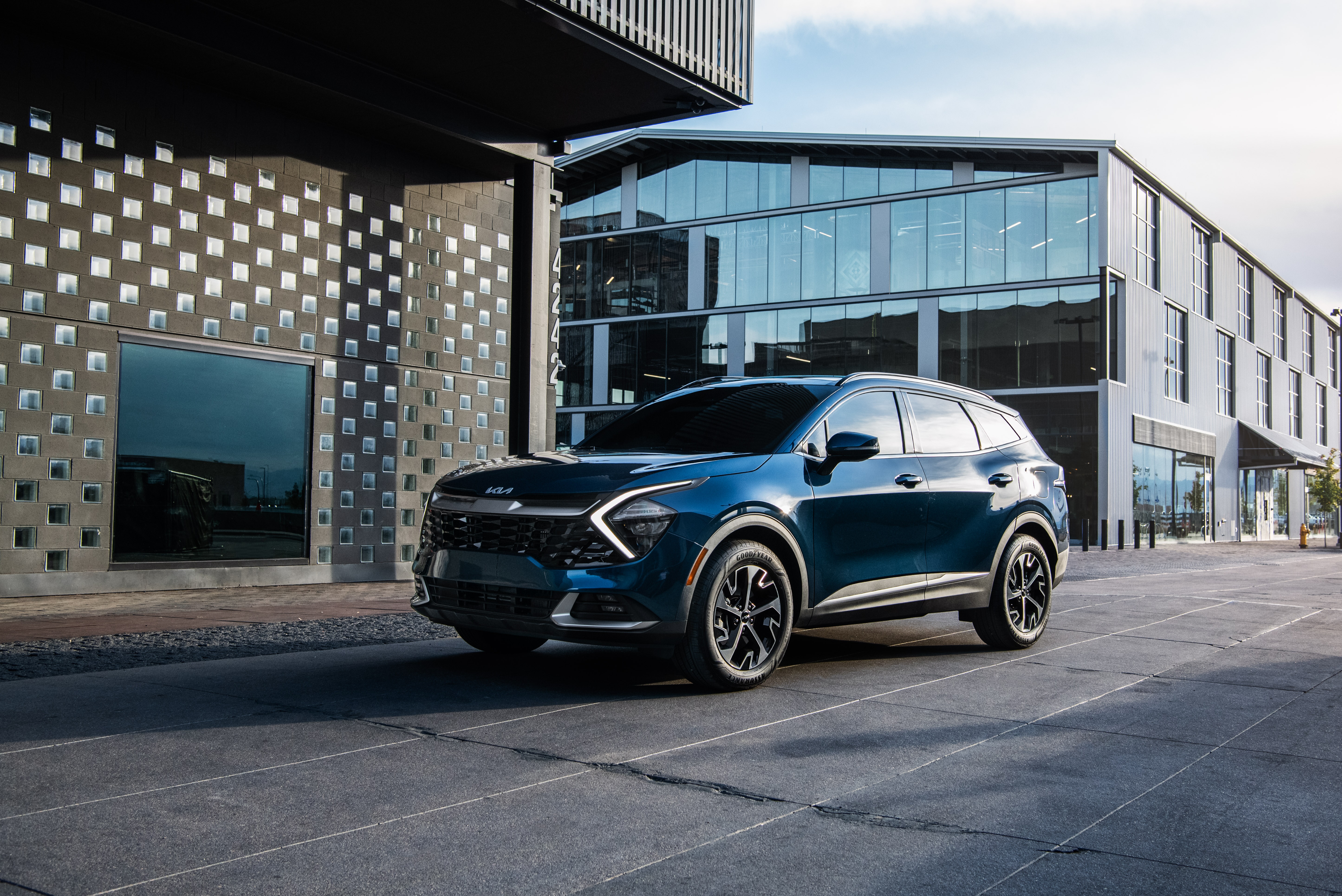 Blue Kia Sportage HEV SUV parked in front of modern buildings HD Wallpaper