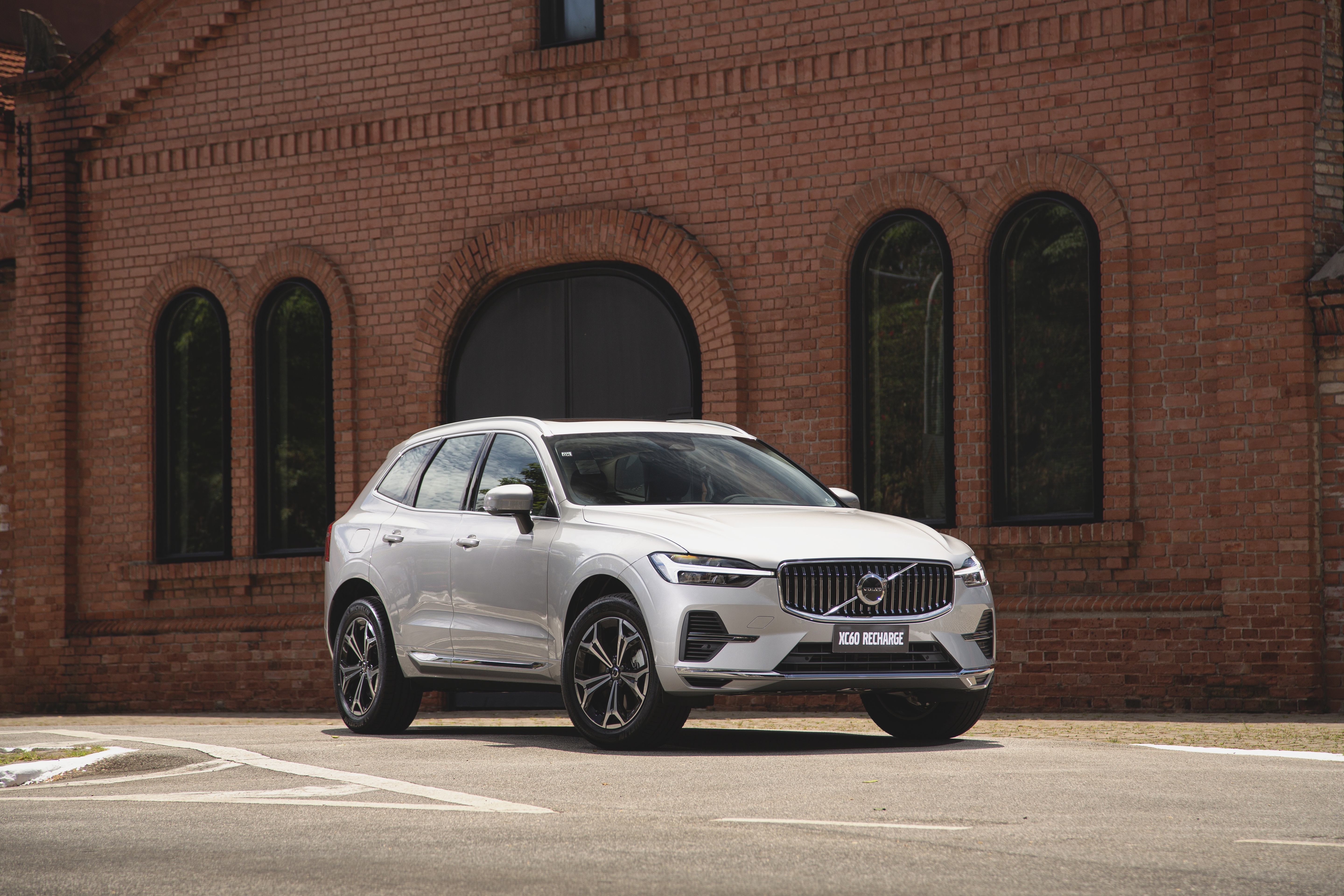 White Volvo XC60 Recharge SUV parked in front of brick building HD Wallpaper