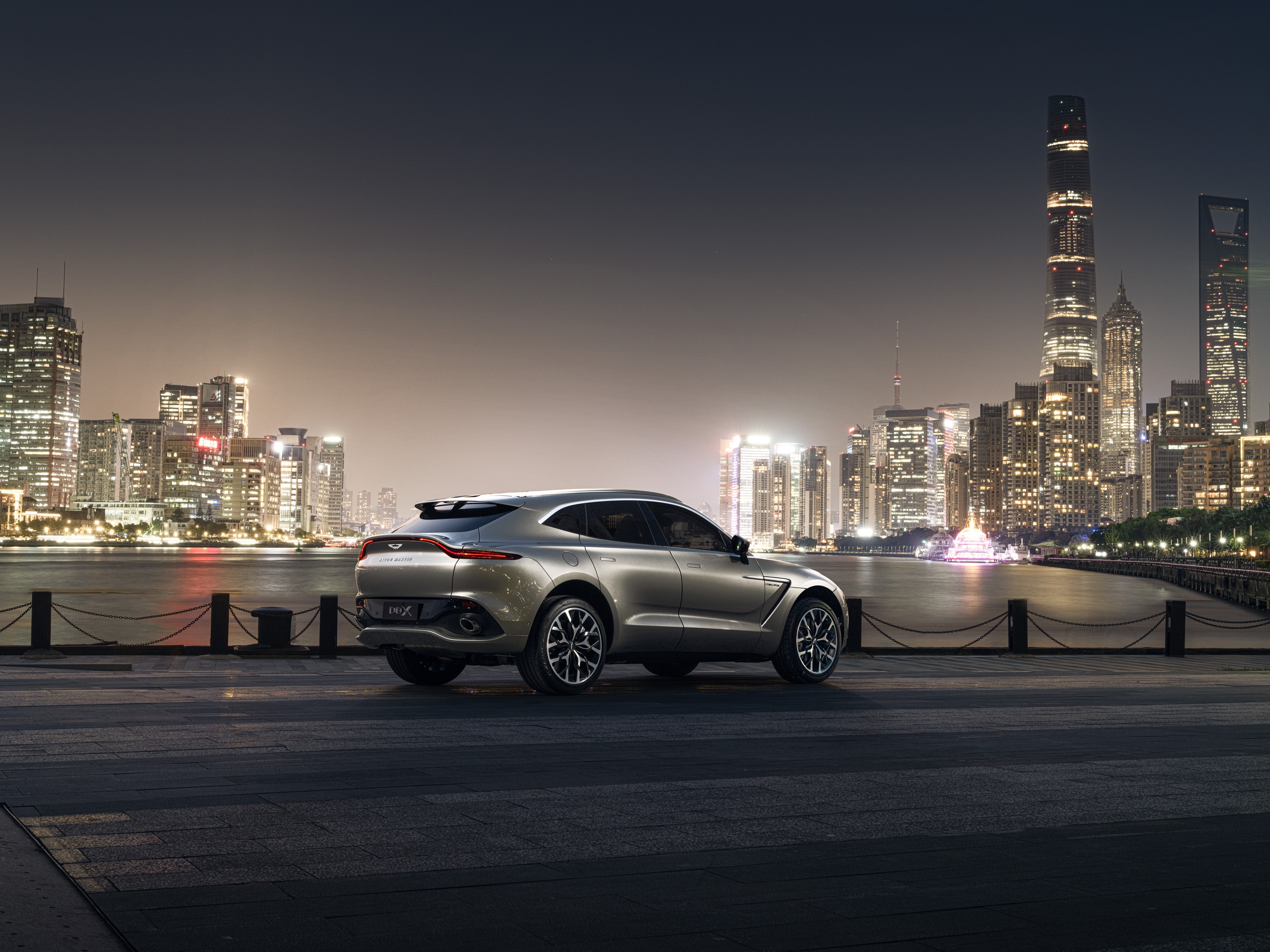 Aston Martin DBX SUV parked by a city skyline at night HD Wallpaper