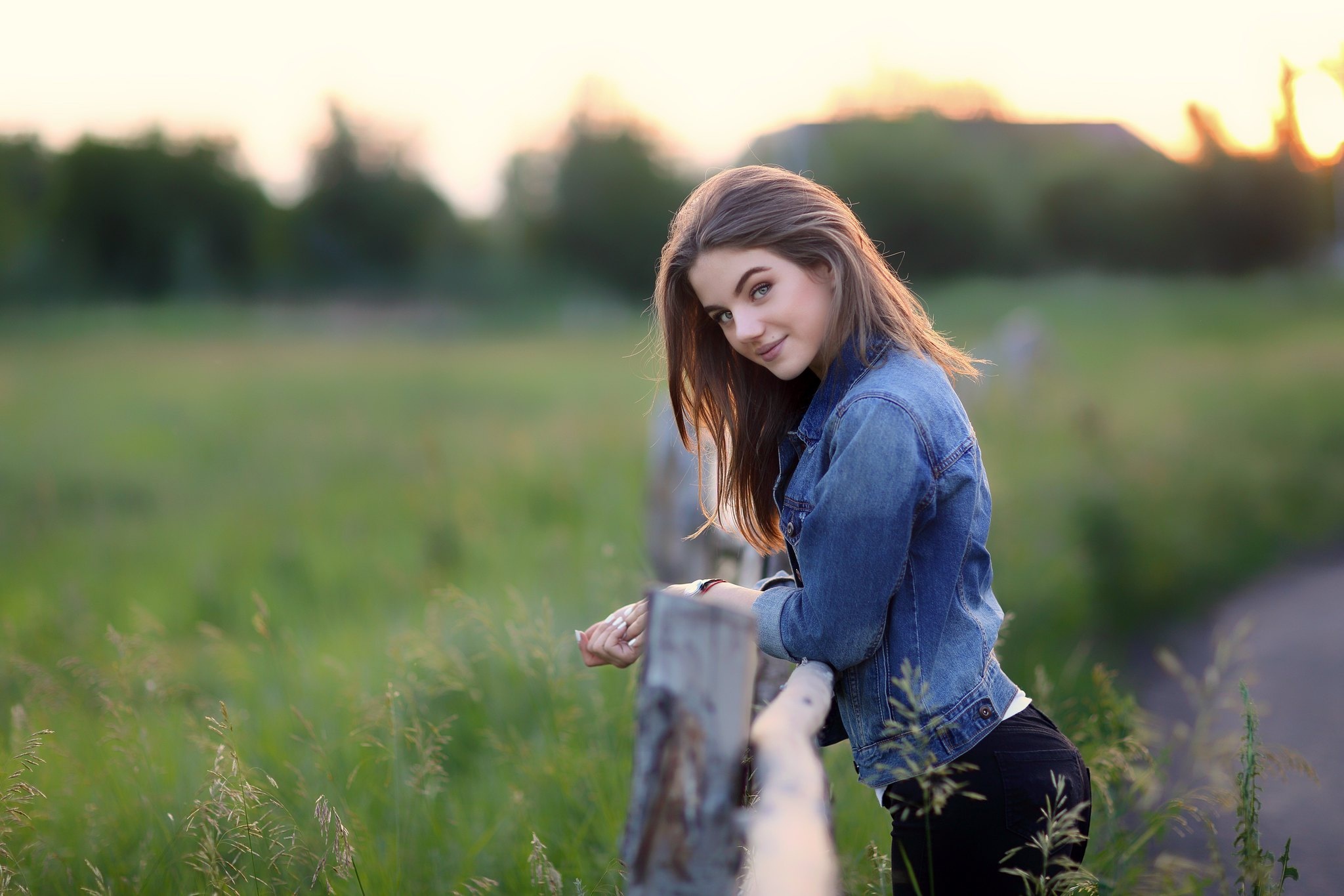 Young woman in denim jacket leaning on fence HD Wallpaper