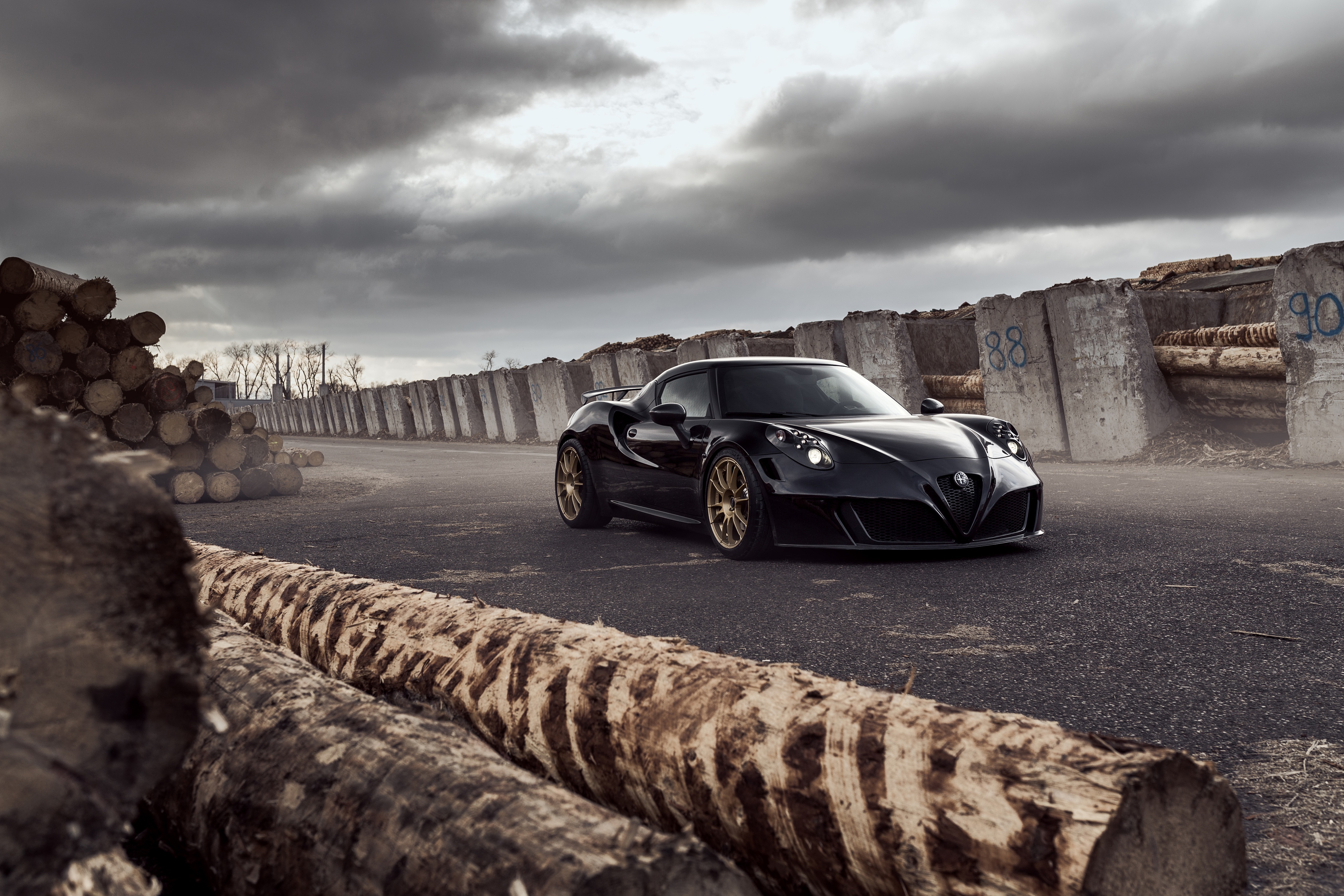 Black Alfa Romeo 4C on asphalt with logs and concrete barriers HD Wallpaper