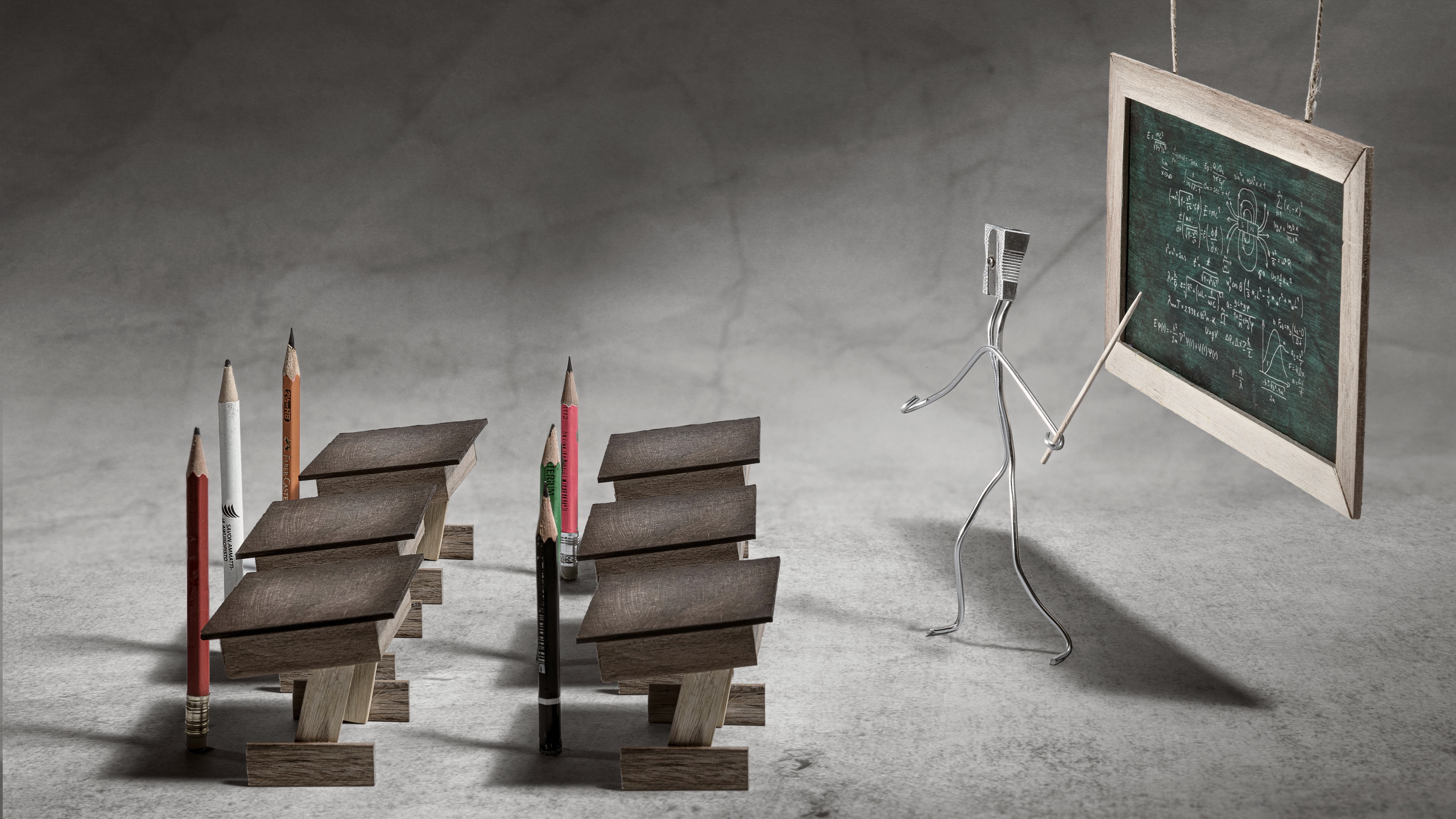 Pencils and desks in a classroom with a wire figure teacher HD Wallpaper