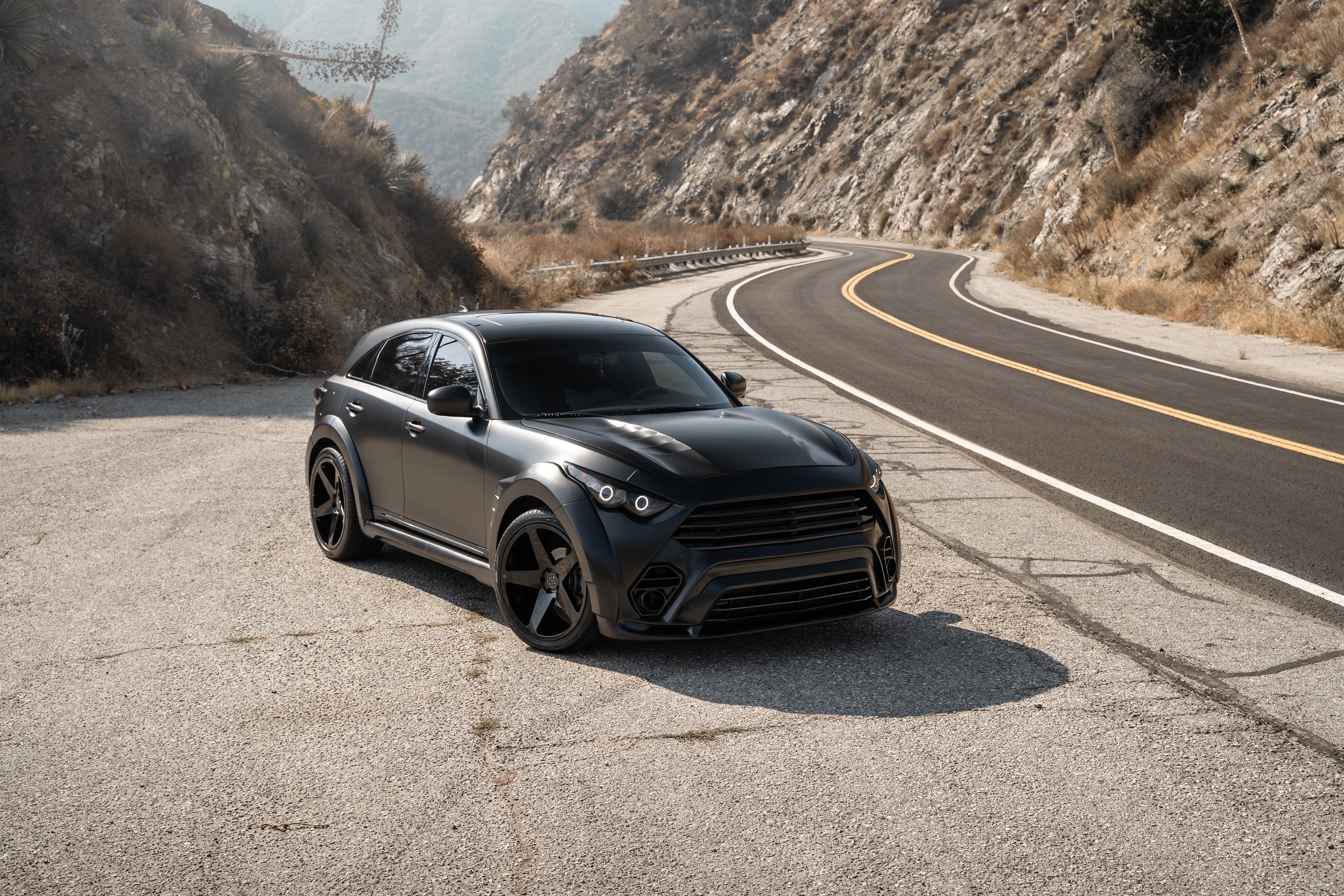 Matte black Infiniti QX70 SUV on a winding mountain road HD Wallpaper