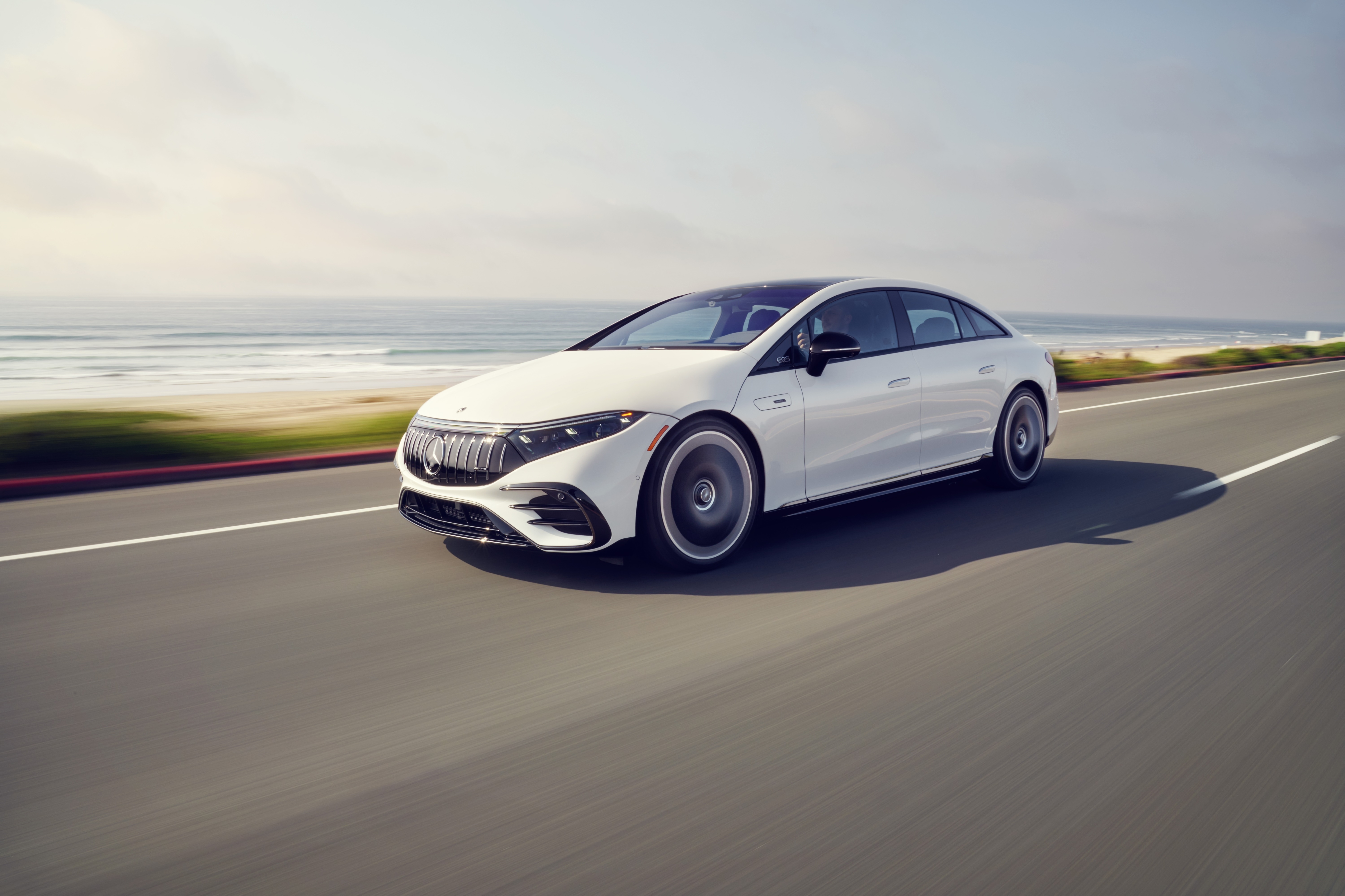 White Mercedes-AMG EQS 53 4MATIC driving on a coastal road HD Wallpaper