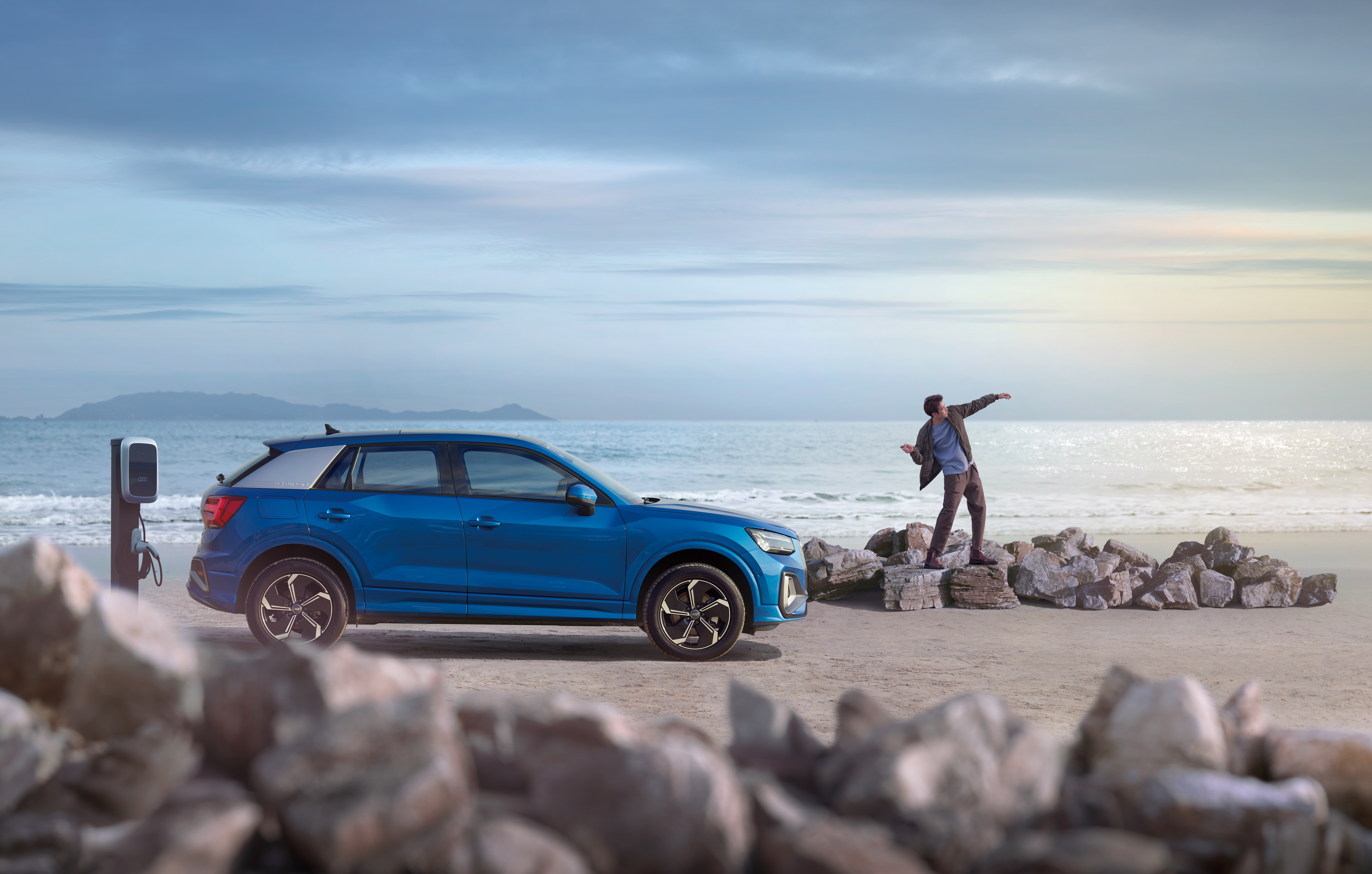 Blue Audi Q2 electric SUV charging on a beach HD Wallpaper