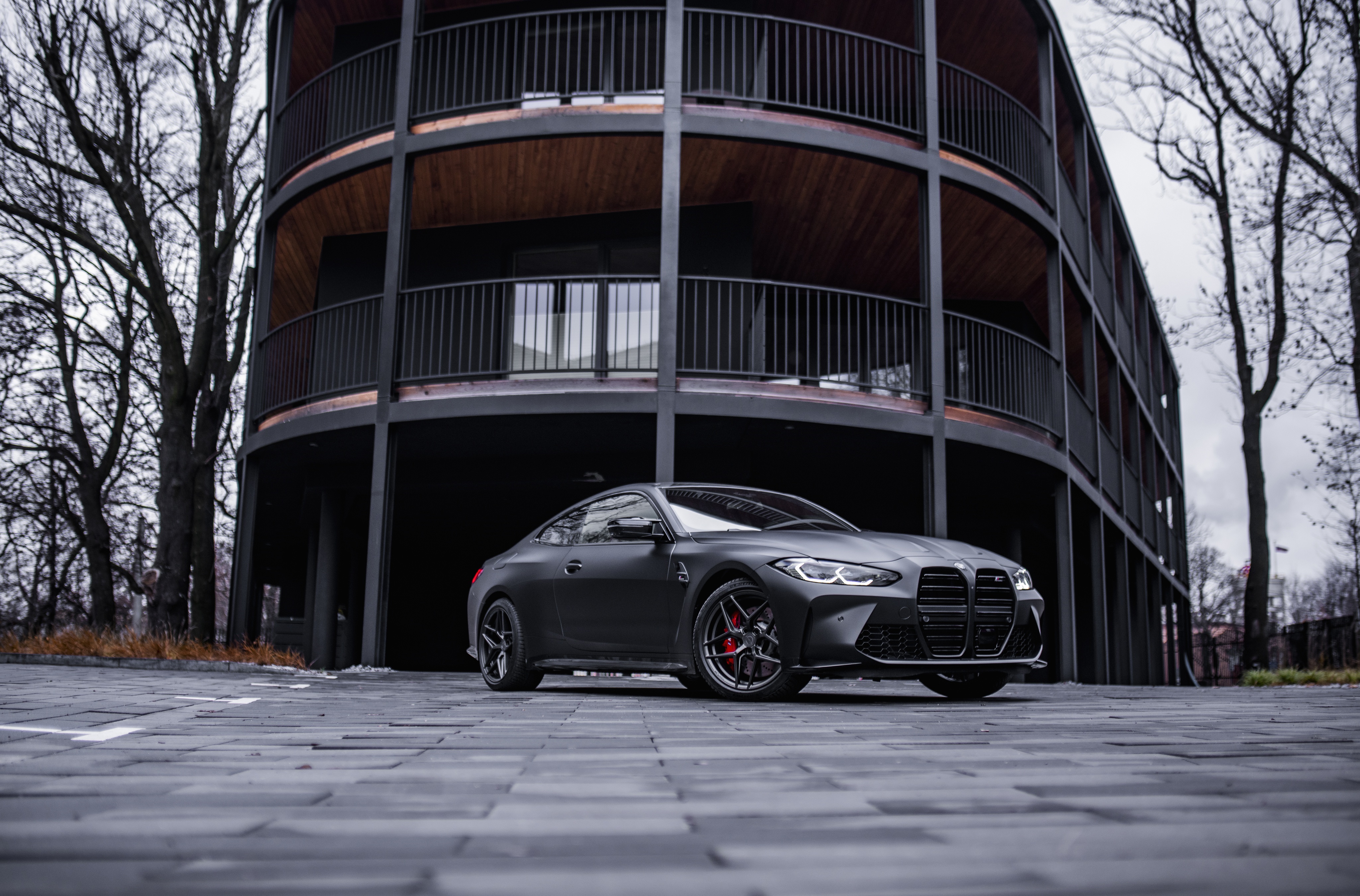 Matte black BMW M4 coupe parked in front of a modern building HD Wallpaper