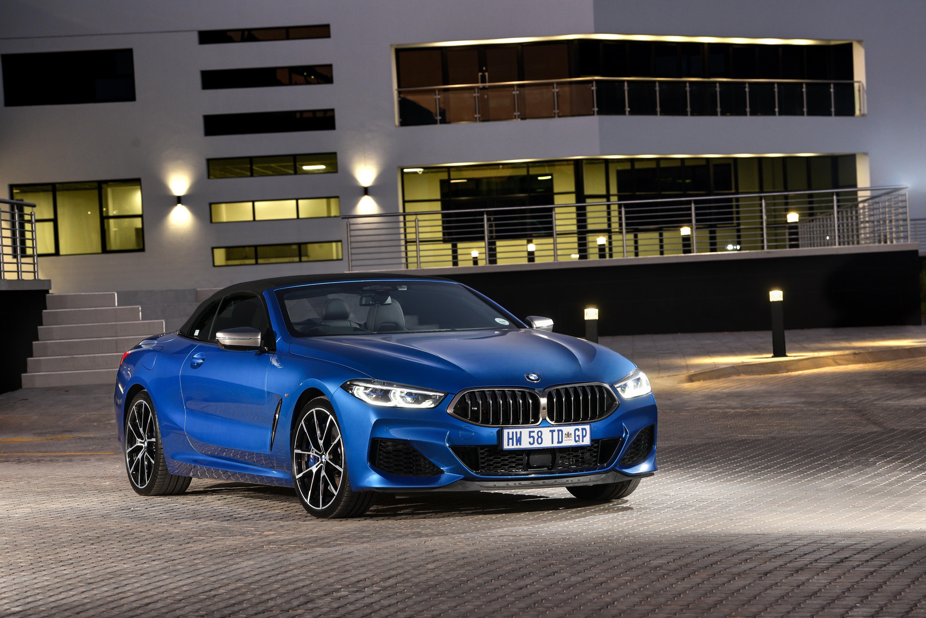 Blue BMW M850i Convertible parked in front of a modern building HD Wallpaper
