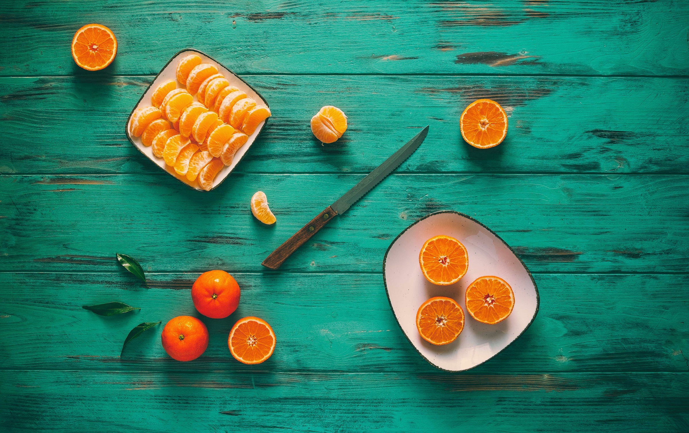 Mandarin slices and whole mandarins on a teal wooden table HD Wallpaper