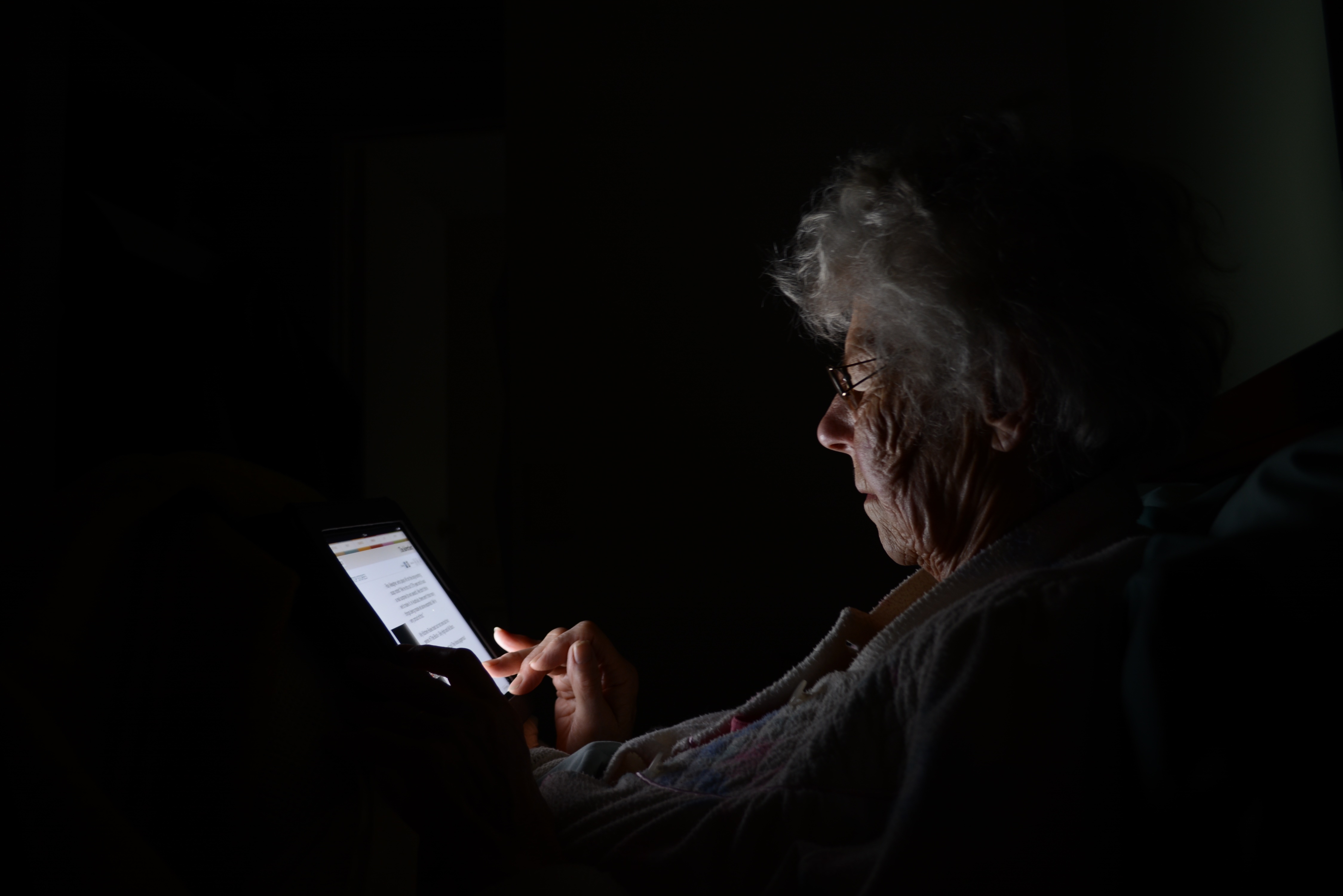 Elderly woman reading on a tablet in the dark HD Wallpaper