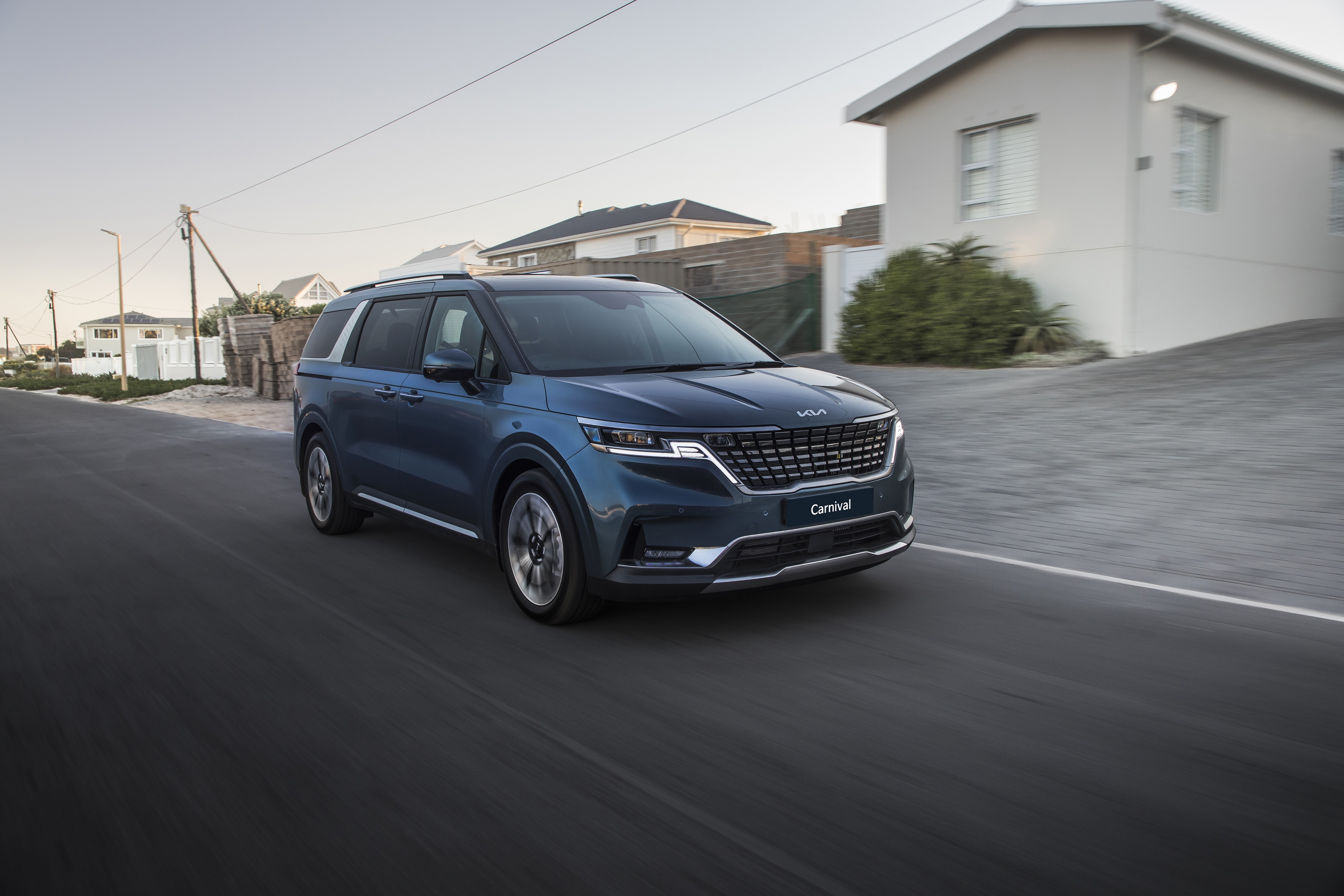 Kia Carnival driving on a suburban street HD Wallpaper