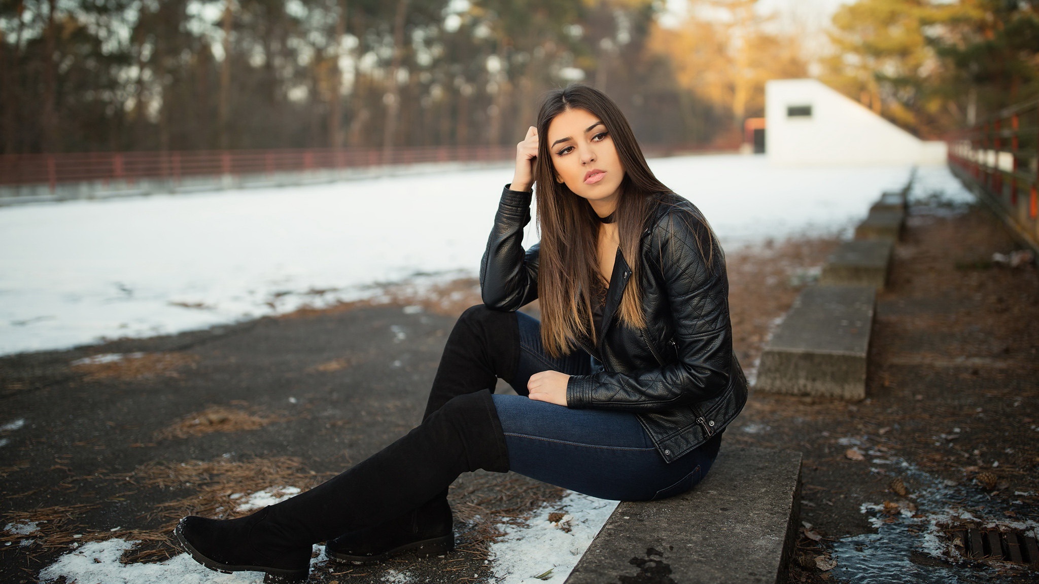 Brunette woman in leather jacket sitting outdoors HD Wallpaper