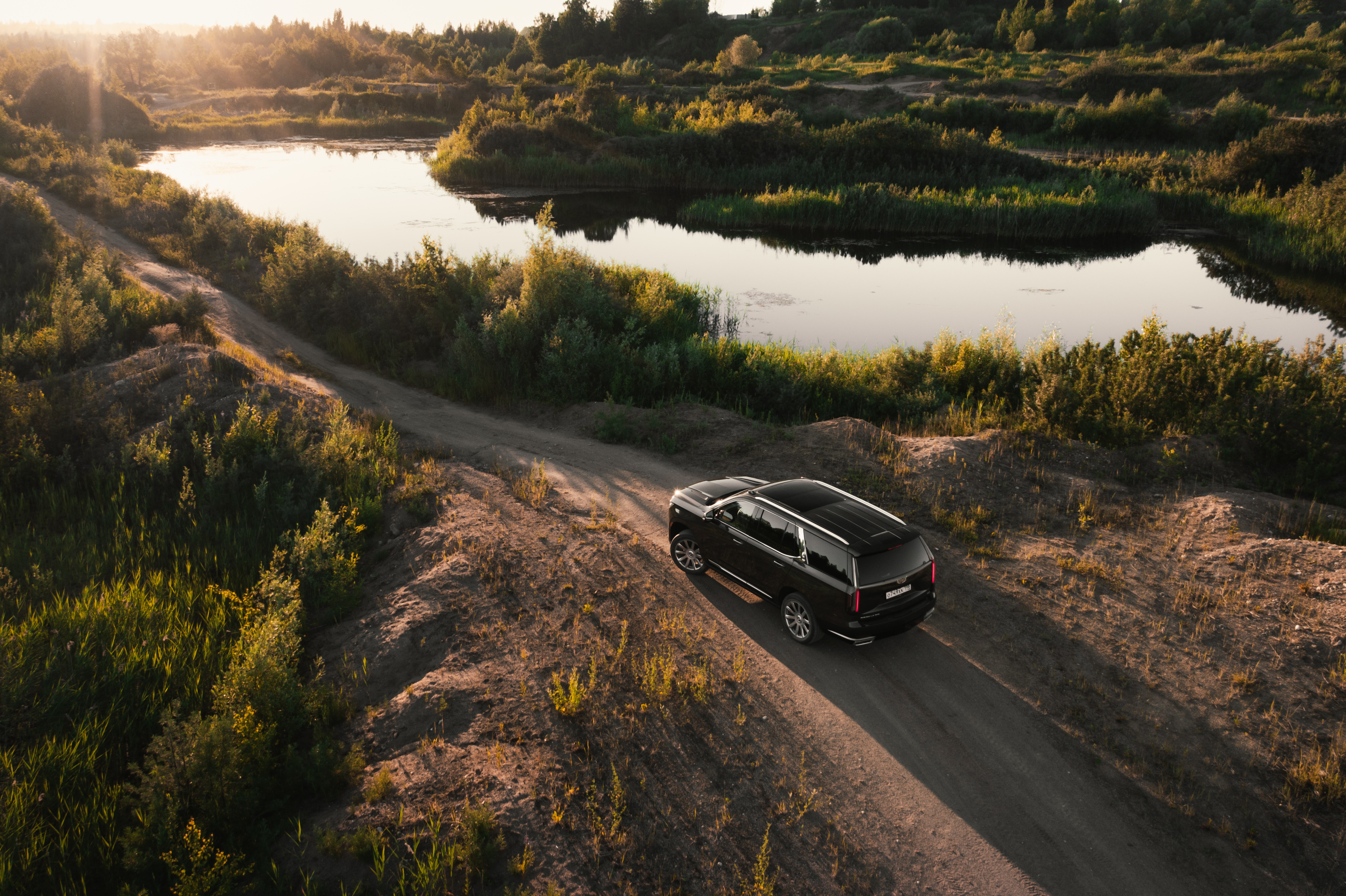 Black Cadillac Escalade on a dirt road near a lake HD Wallpaper