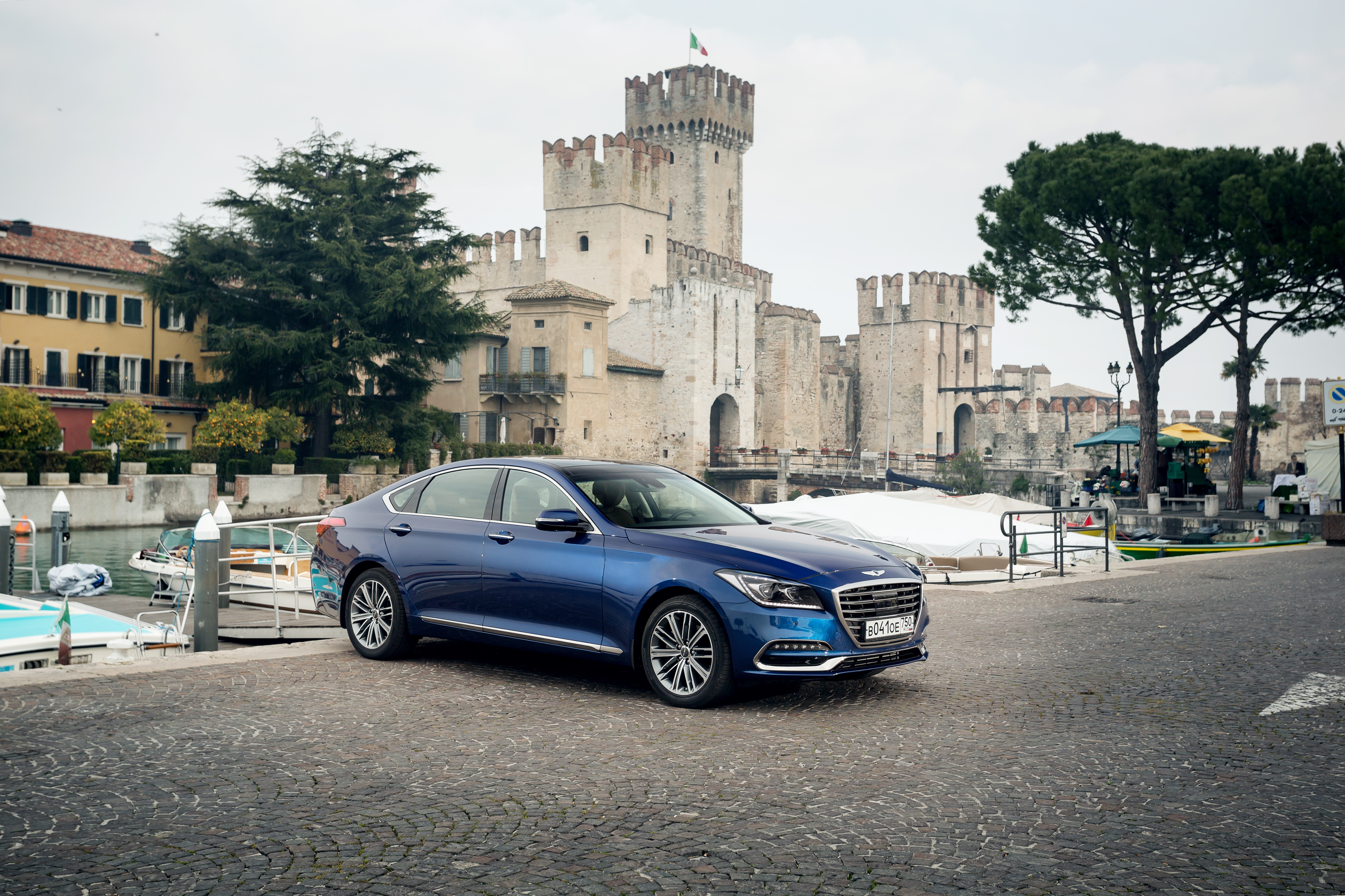 Blue Genesis G80 Sedan parked near a castle and harbor HD Wallpaper