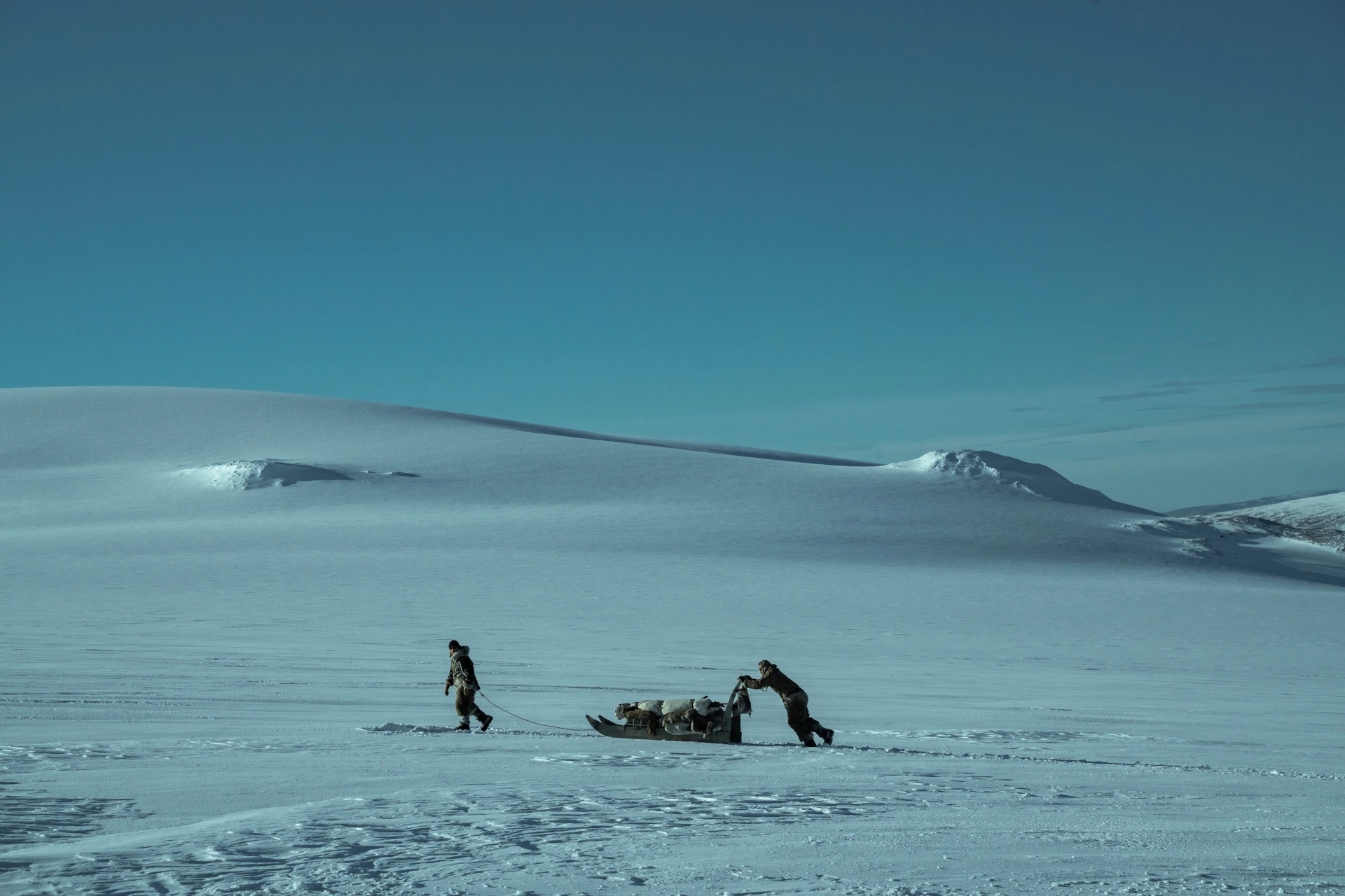 Two people pulling a sled across a snowy landscape HD Wallpaper