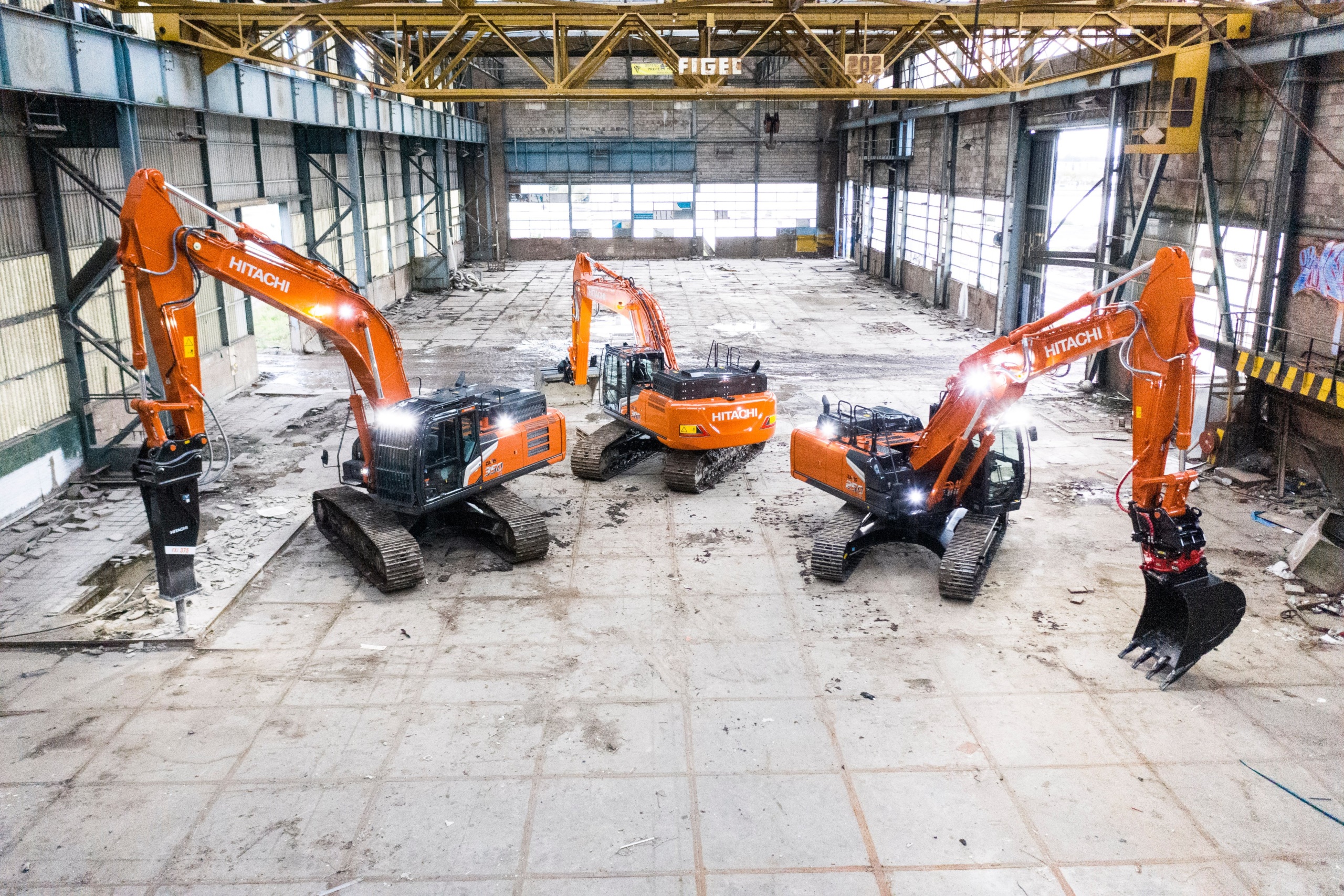 Three Hitachi excavators in a large industrial building HD Wallpaper
