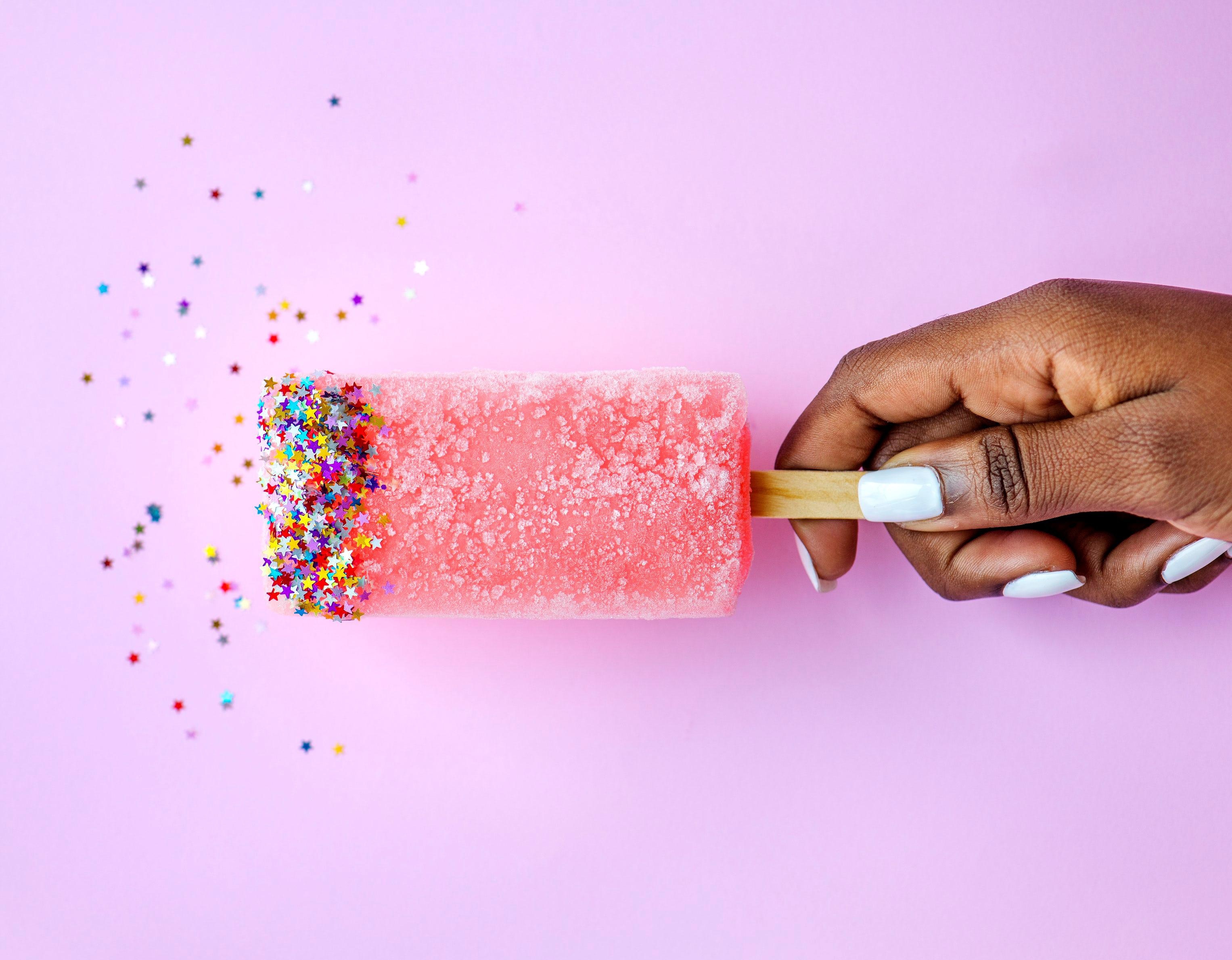 Hand holding a pink popsicle with star sprinkles HD Wallpaper