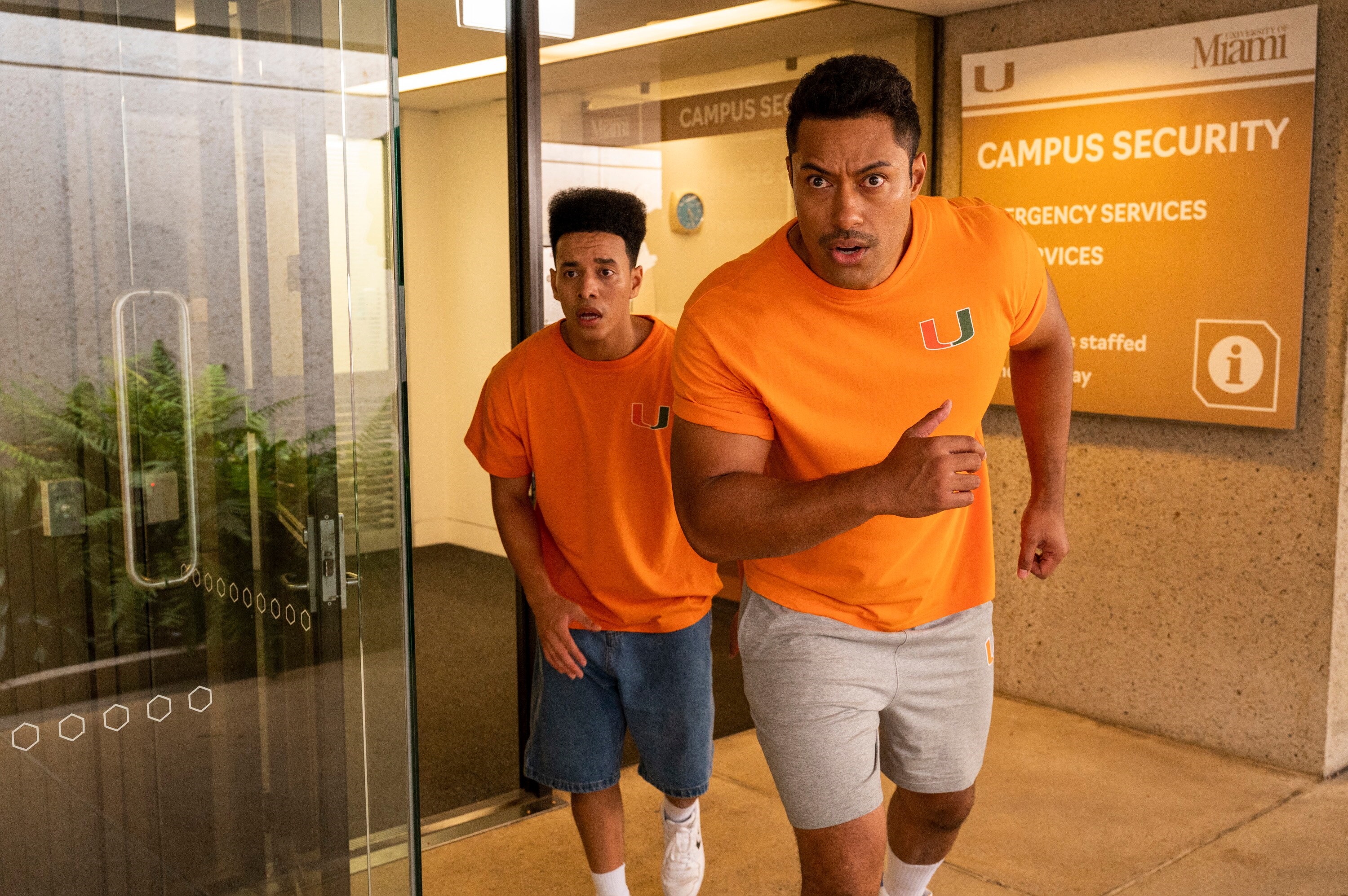 Two men in orange shirts running near campus security sign HD Wallpaper