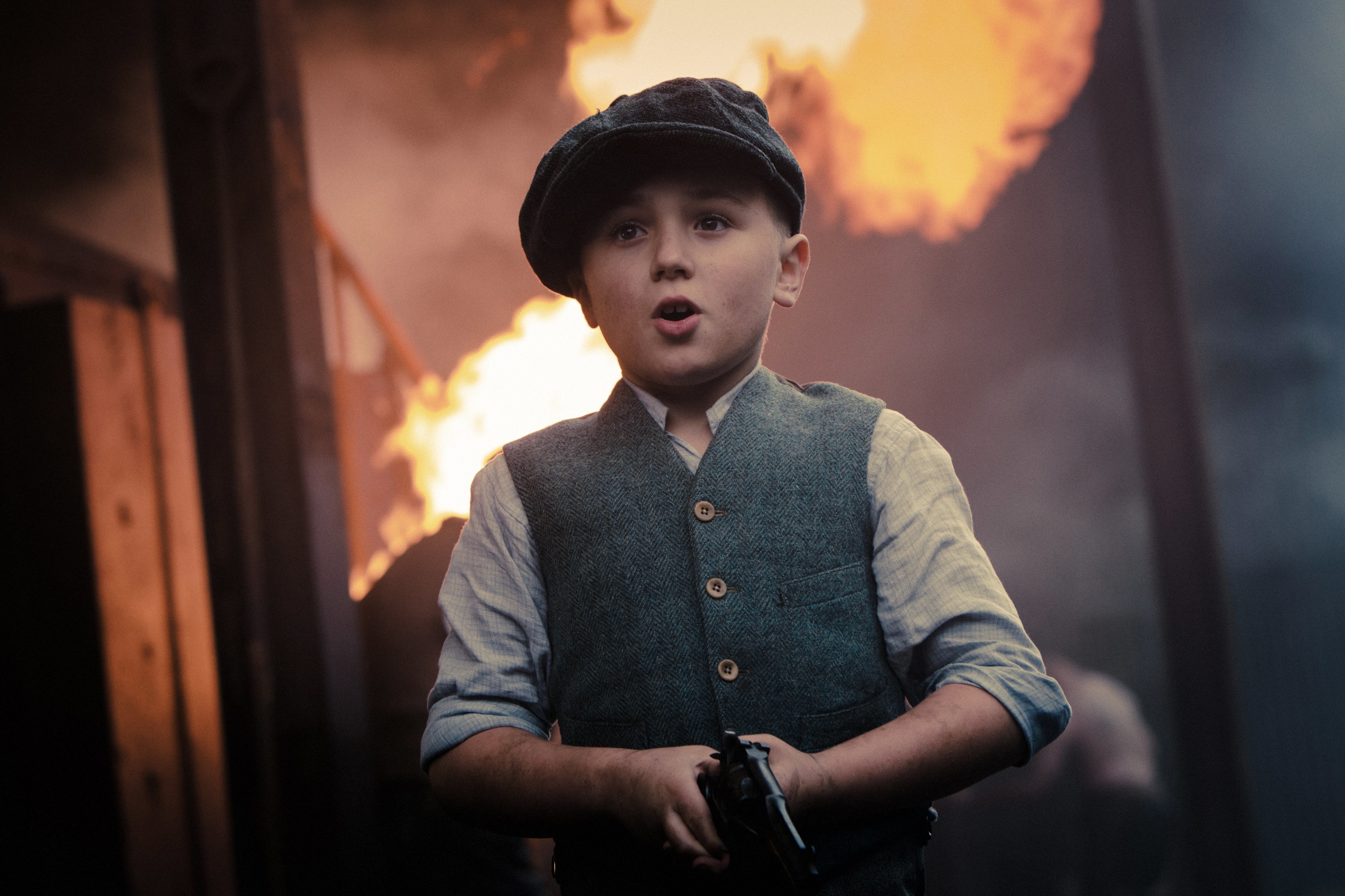 Young boy from Peaky Blinders holding a gun with fire in background HD Wallpaper
