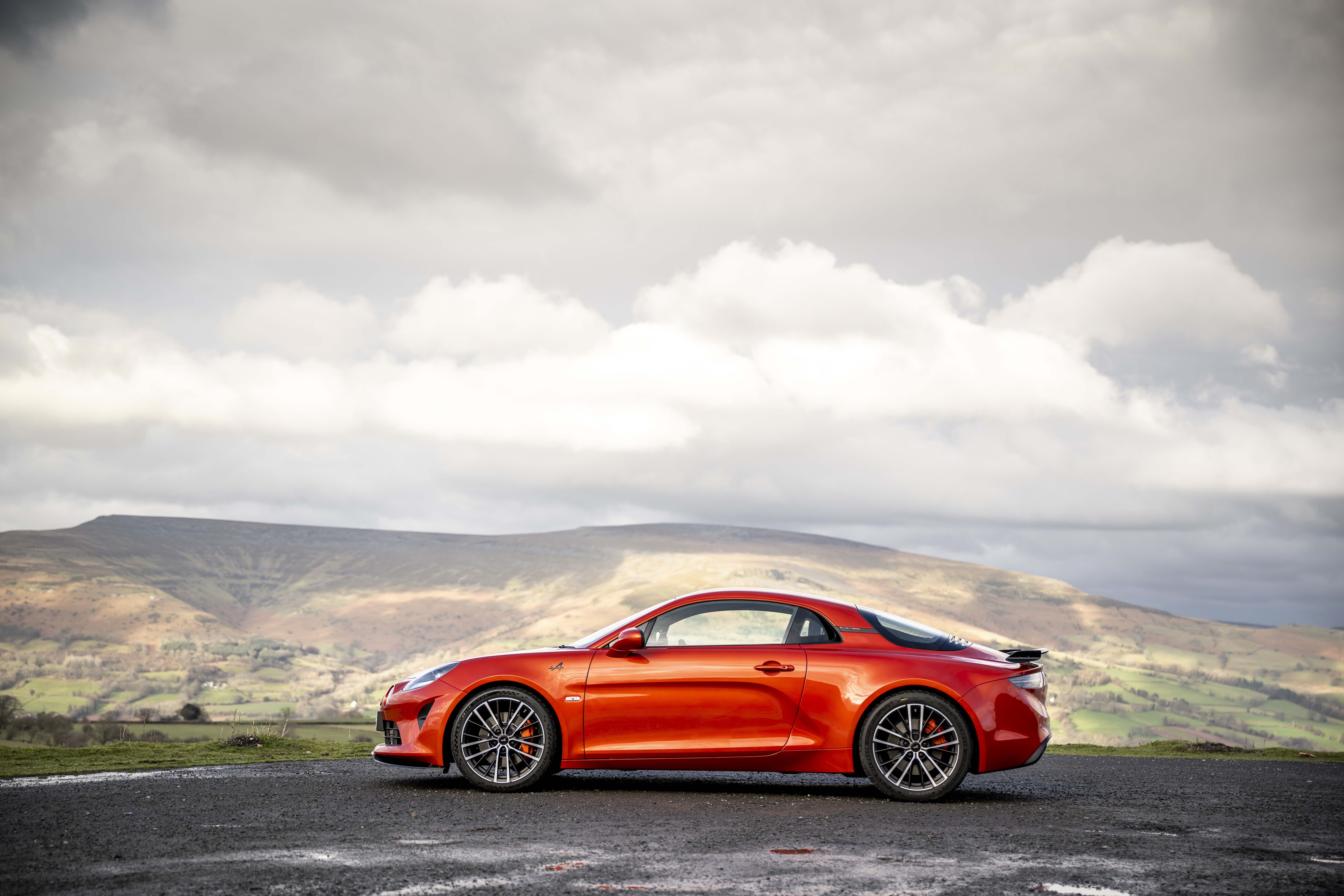 Orange Alpine A110S sports car on a road with mountains HD Wallpaper
