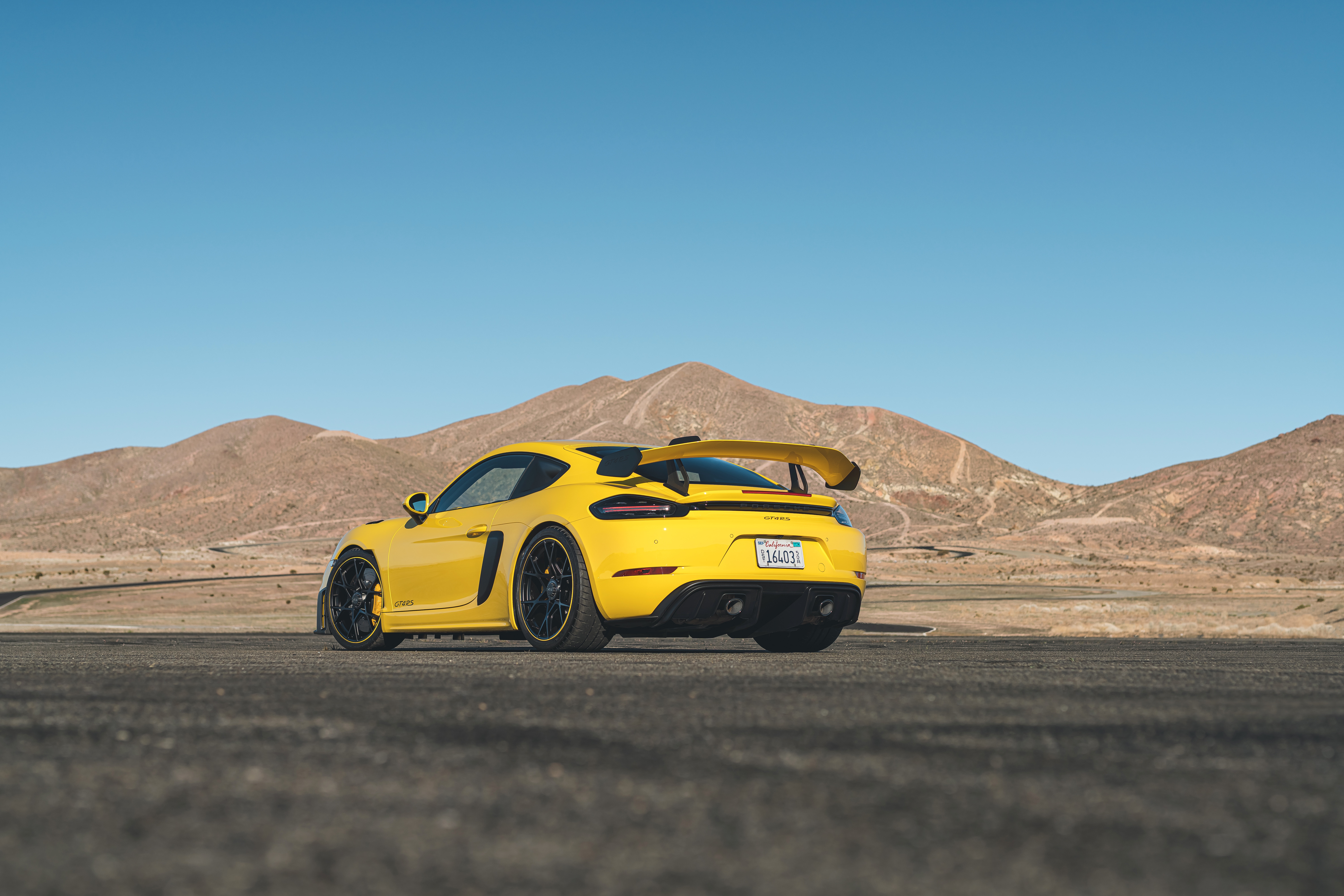 Yellow Porsche 718 Cayman GT4 in desert landscape HD Wallpaper