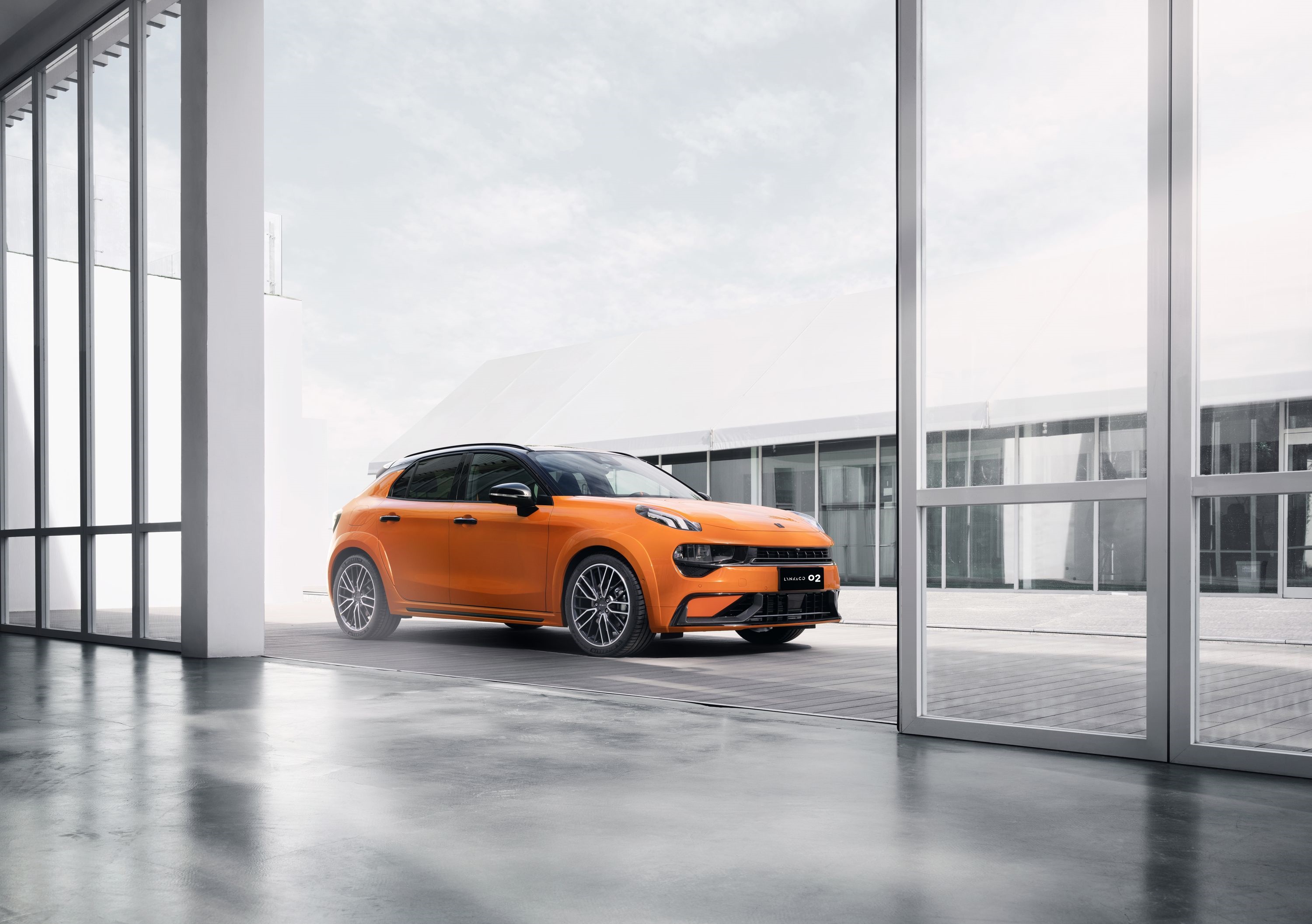 Orange Lynk & Co 02 Hatchback parked outside modern building HD Wallpaper