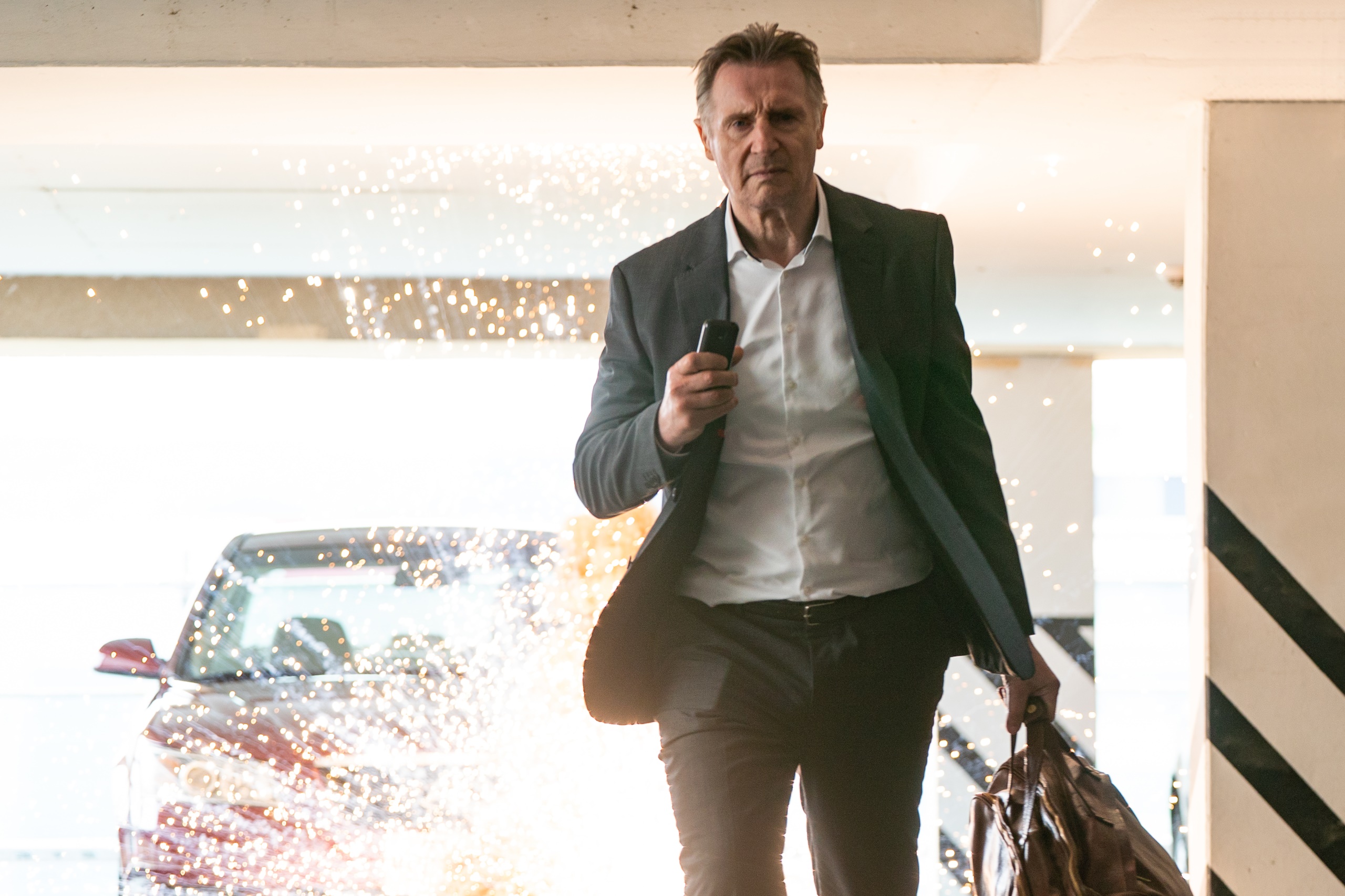 Liam Neeson in a suit holding a phone and bag HD Wallpaper