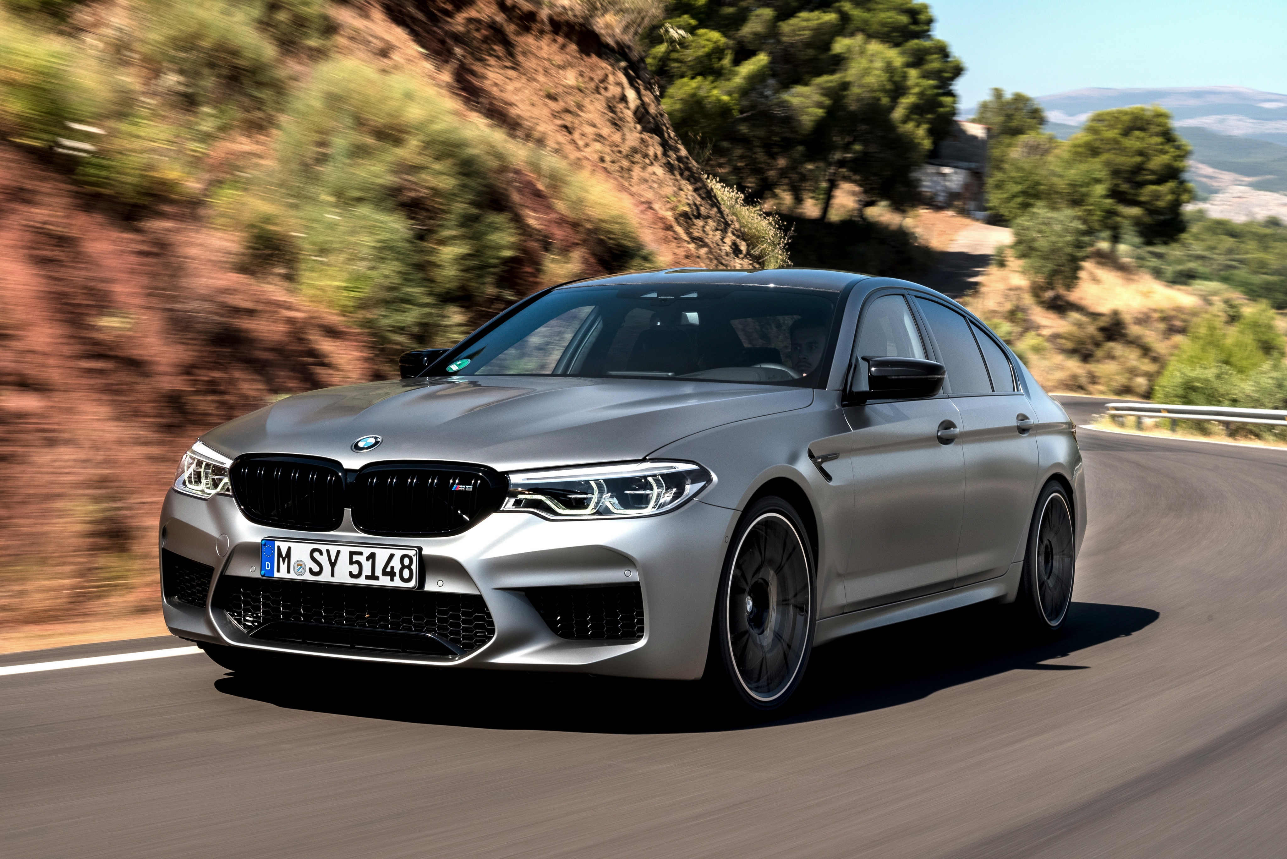 Silver BMW M5 Competition driving on a winding road HD Wallpaper