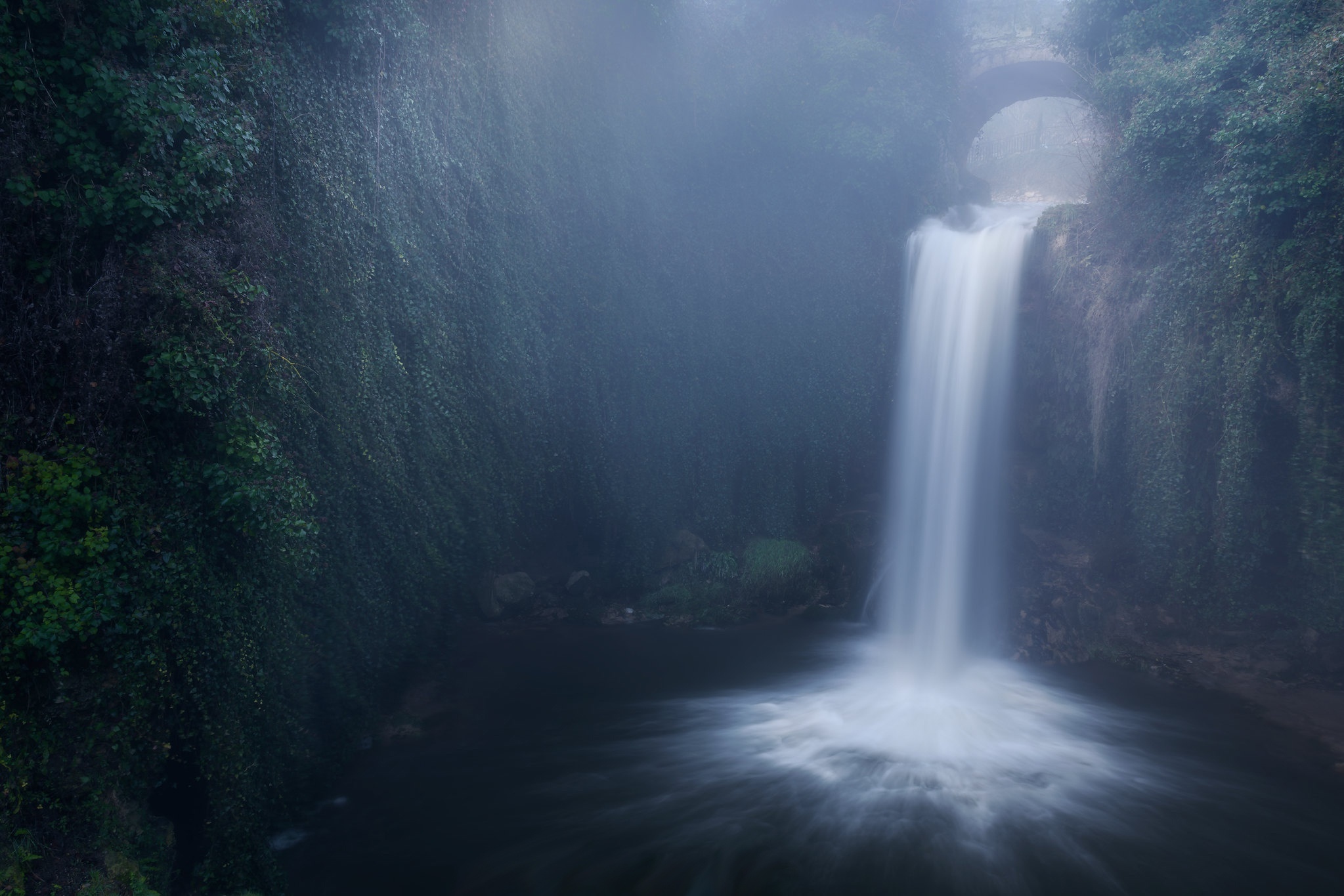 Waterfall flowing under a stone bridge HD Wallpaper